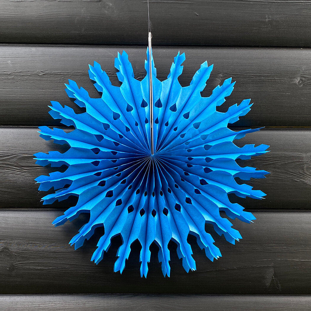 Bright blue paper snowflake decoration with cut-out details, hanging against a dark wood background.