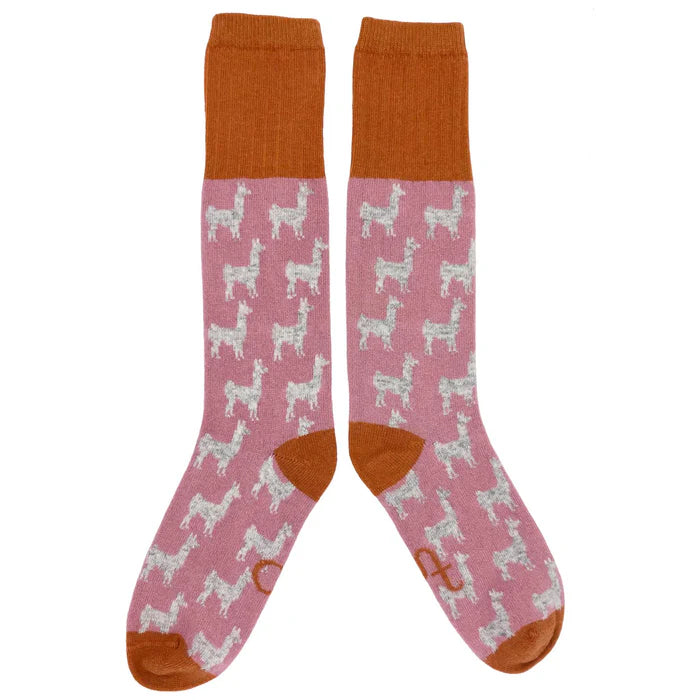 Pair of pink crew socks featuring a repeating pattern of gray llamas.  The socks have burnt orange cuffs and toes.