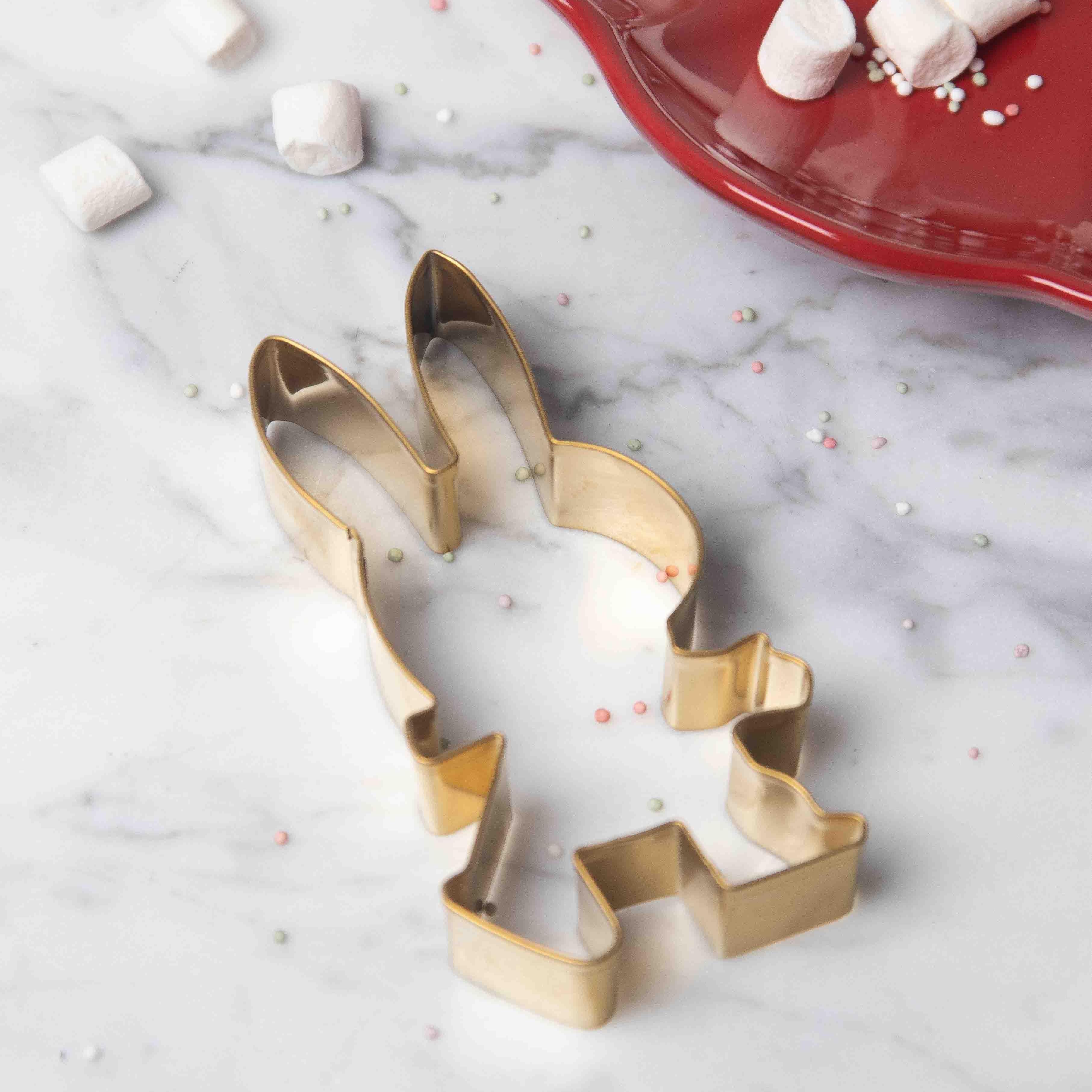 Gold rabbit-shaped cookie cutter on a marble surface.