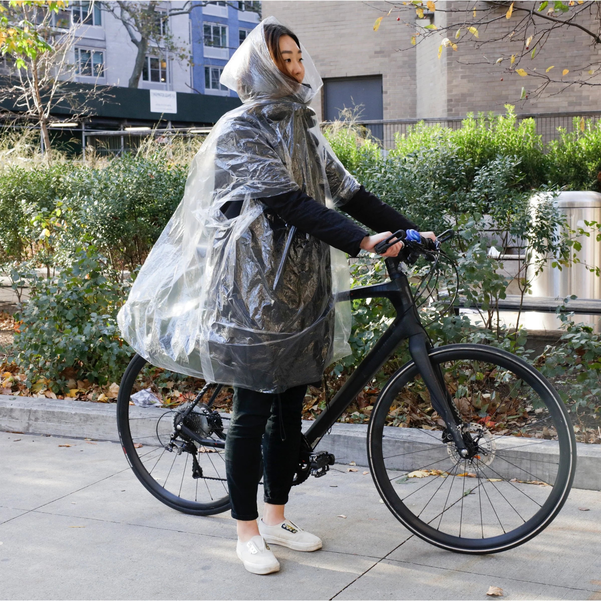 Person wearing a clear plastic poncho while riding a black bicycle.