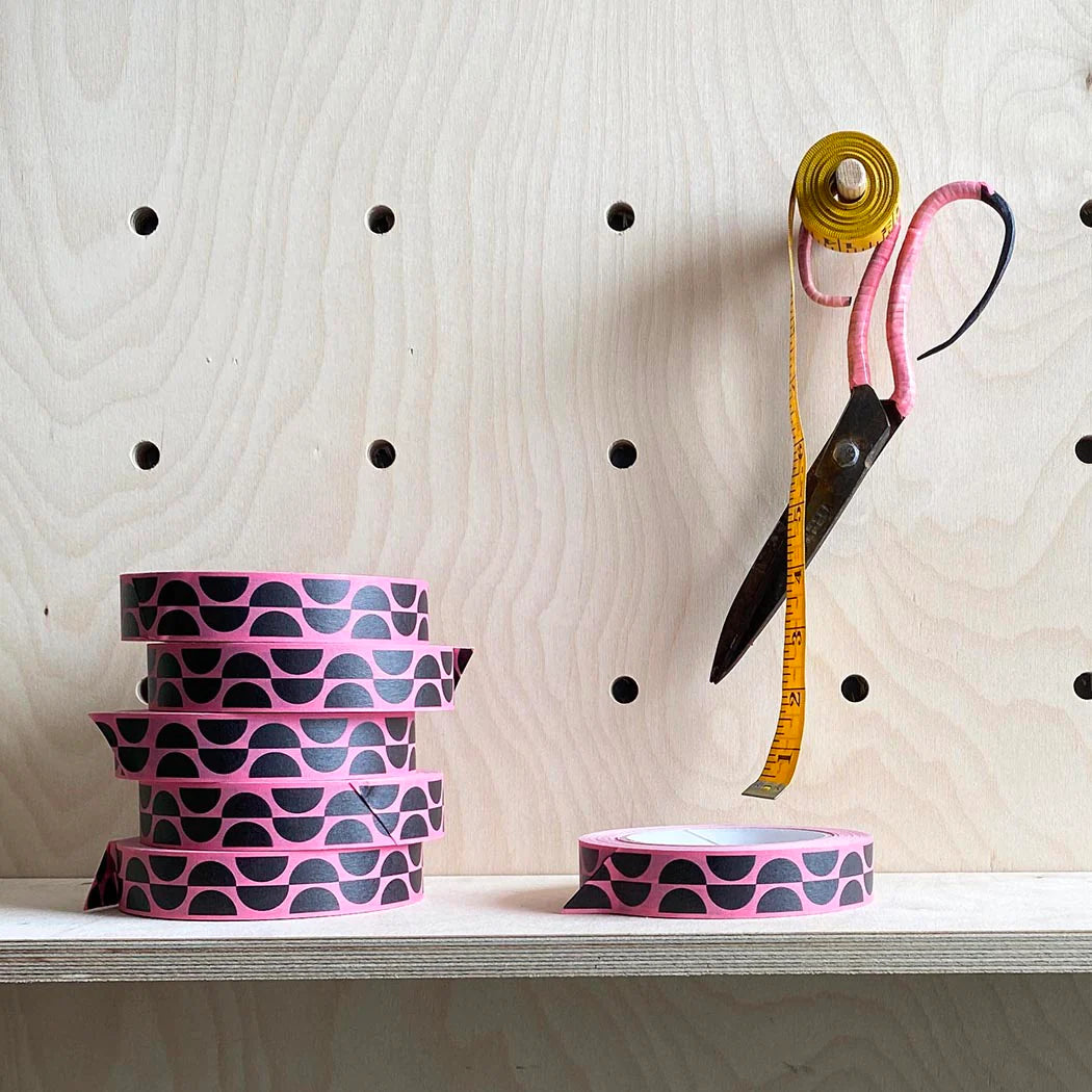Pink washi tape rolls with a black semi-circle pattern. A yellow tape measure and pink scissors are also shown.