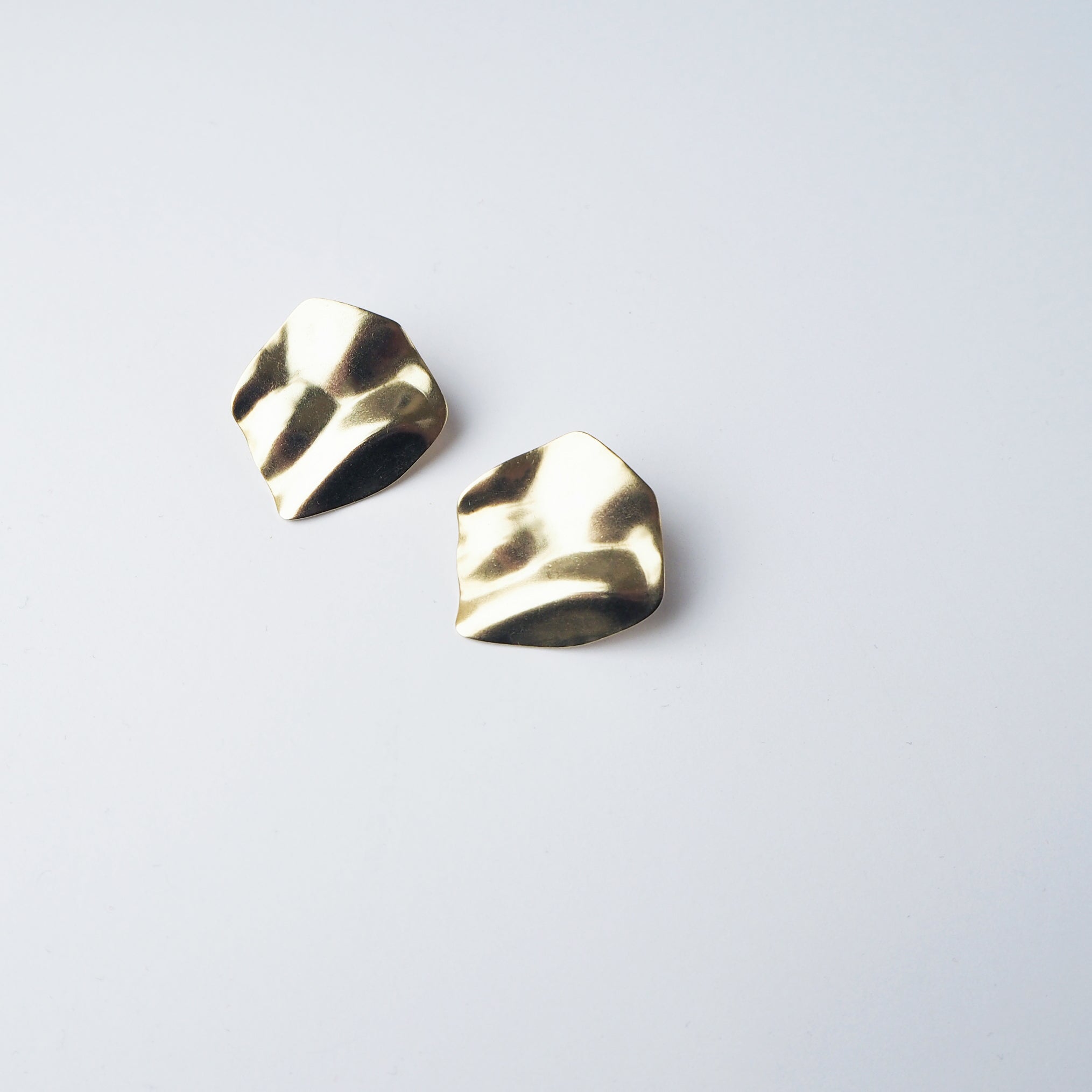 Pair of gold, textured, irregular-shaped earrings.  The earrings have a hammered or crumpled metallic finish.