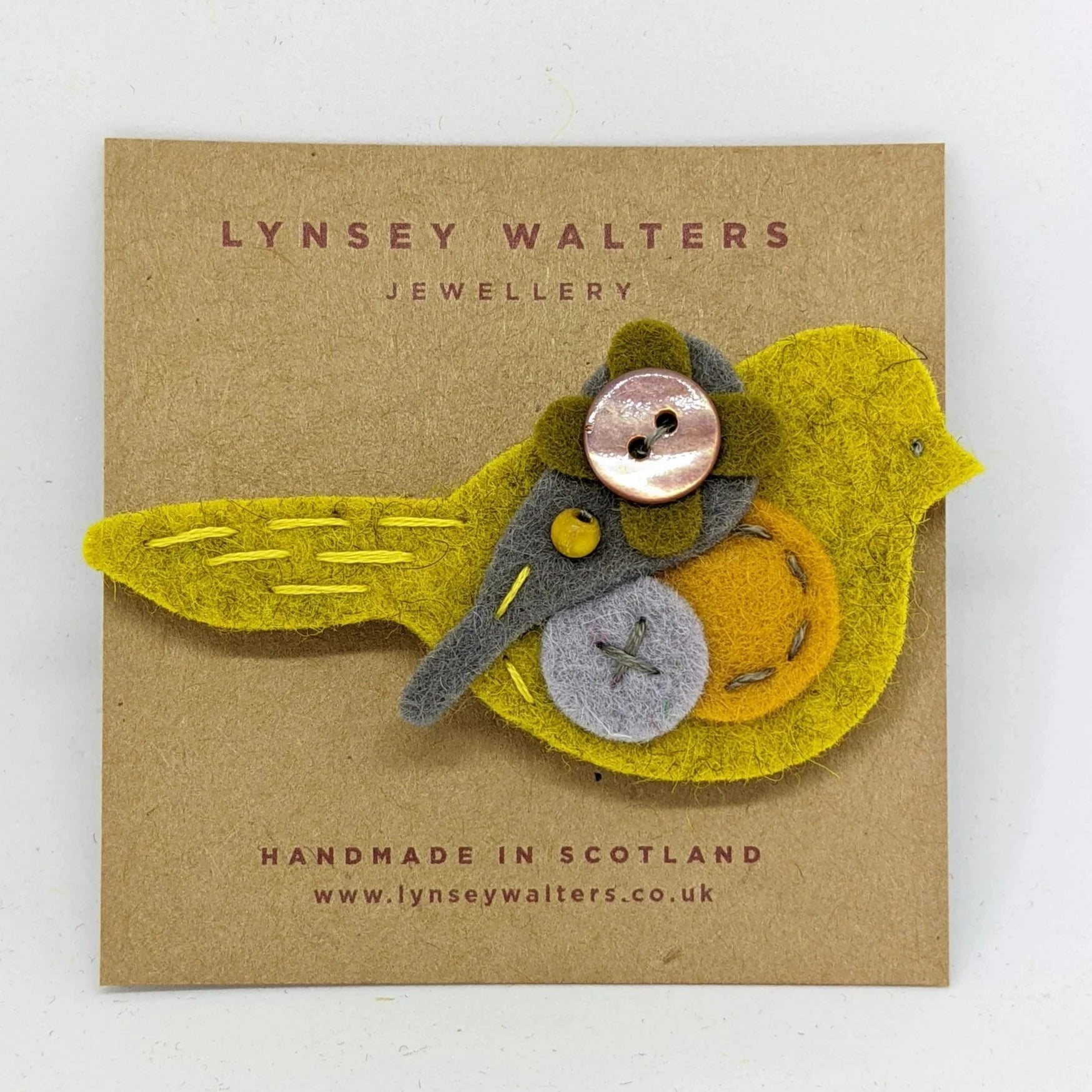 Handmade felt bird brooch in yellow, gray, and orange, featuring decorative buttons and stitching.
