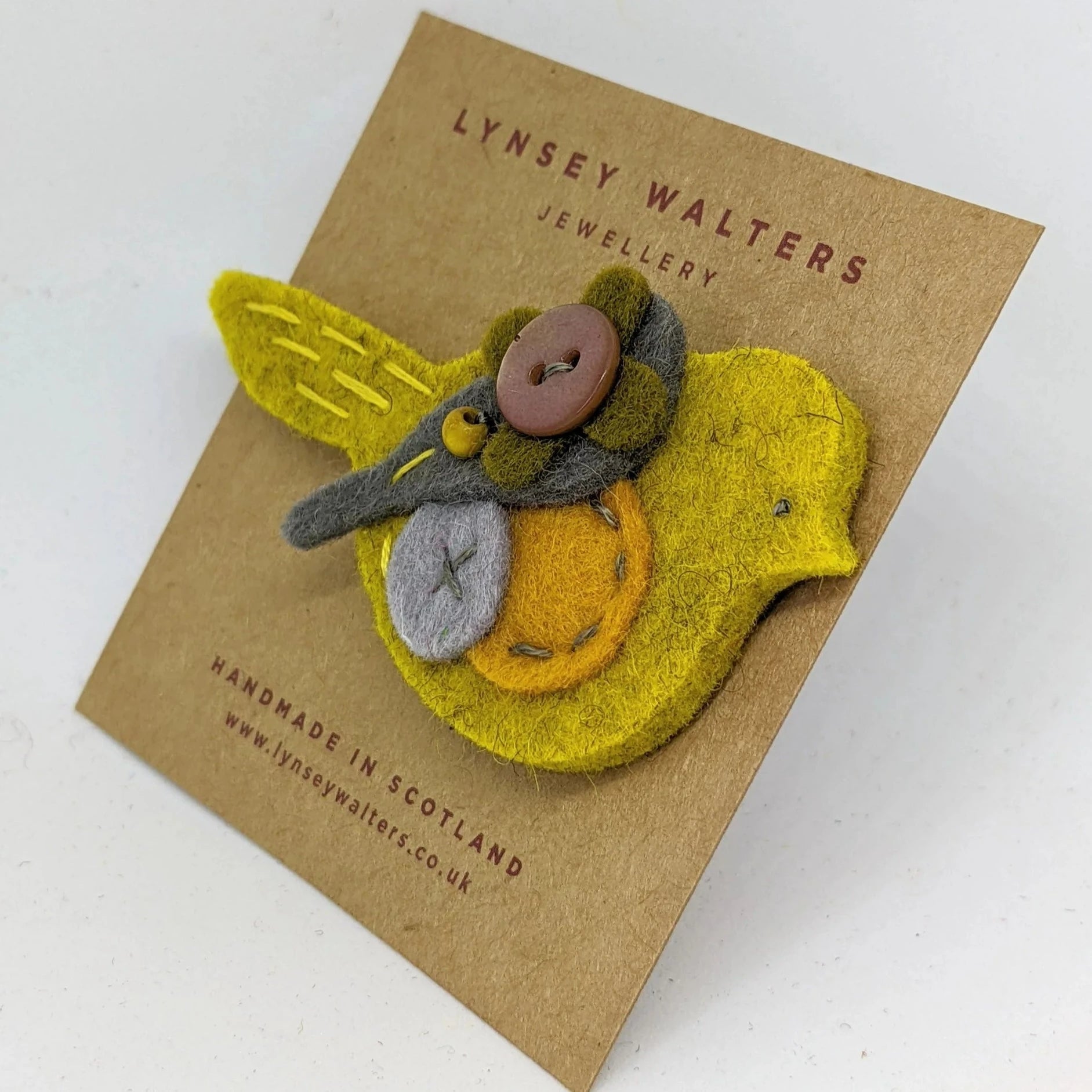 Handmade felt bird brooch in yellow, gray, and orange, with buttons as accents.