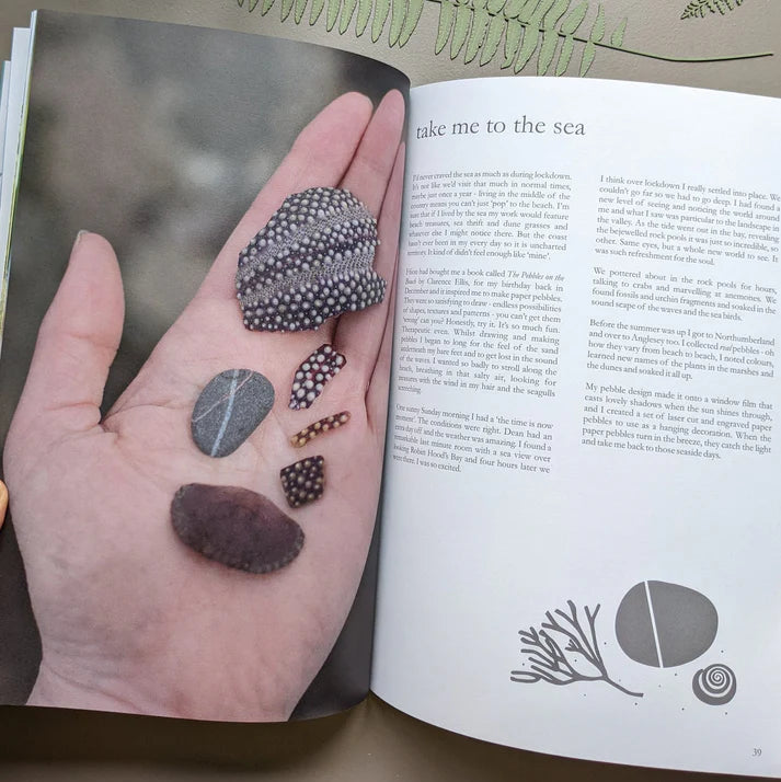 Hand holding several smooth, patterned sea pebbles; some dark, others speckled white.