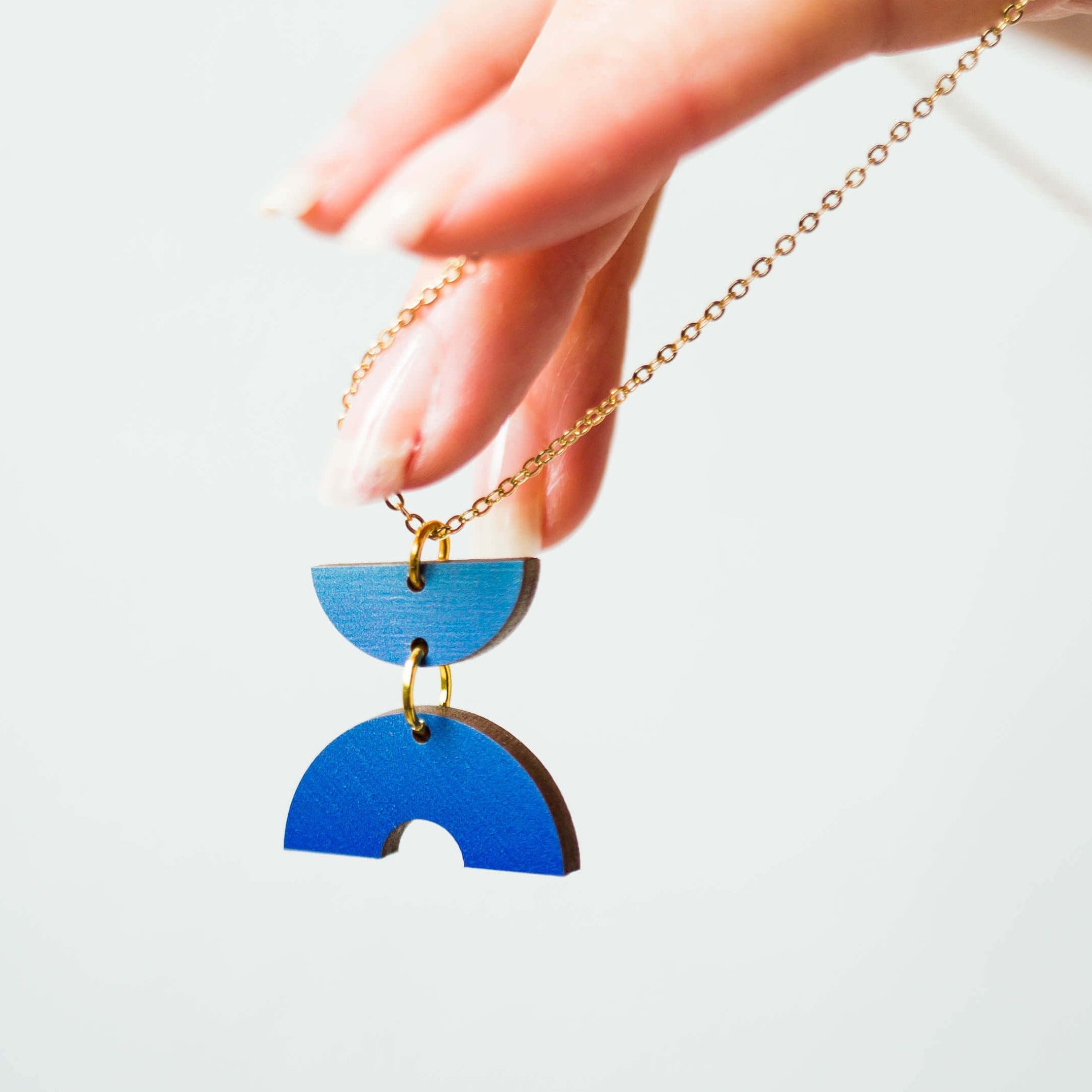 Gold chain necklace with a blue, geometric, wooden pendant featuring two stacked semicircle shapes.