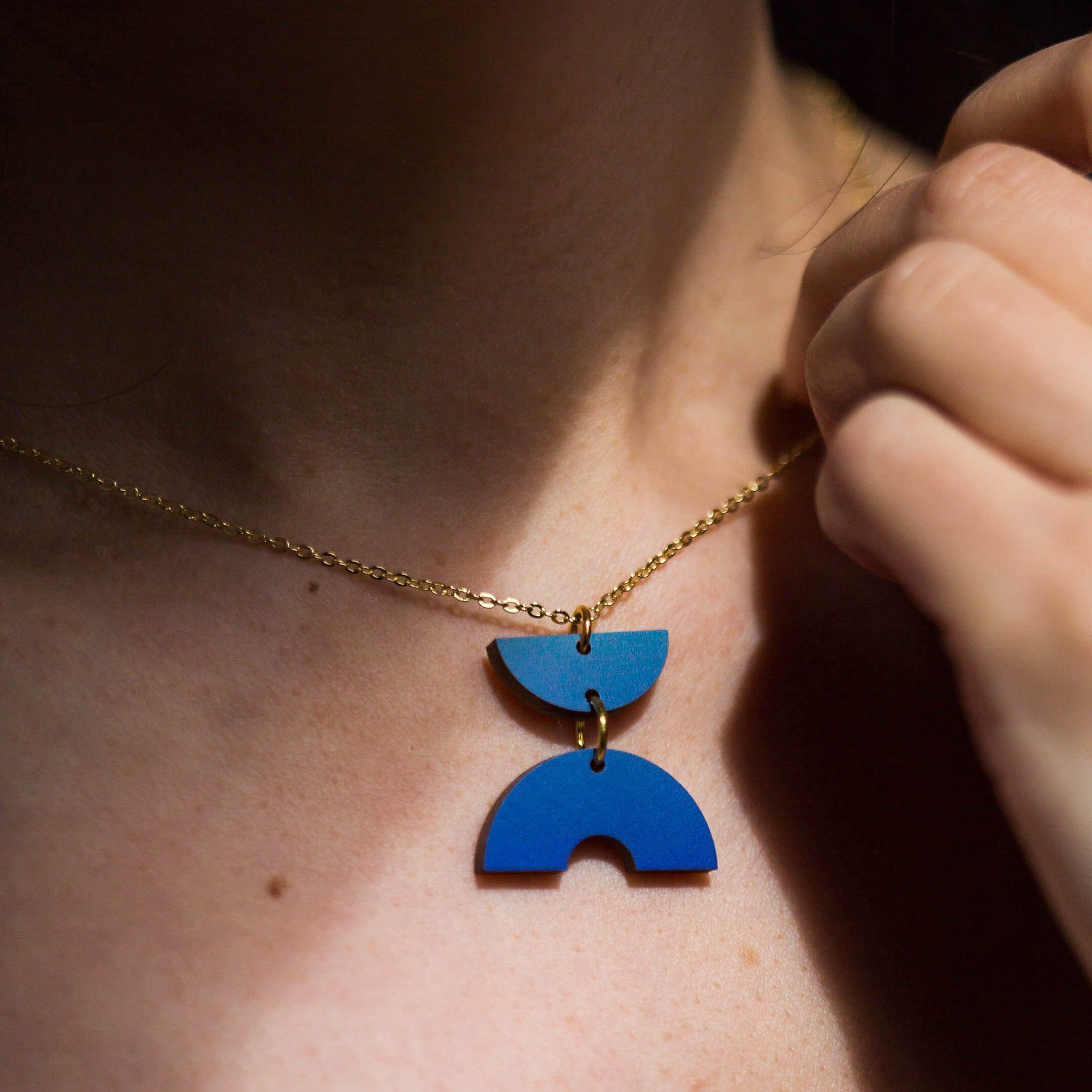 Gold chain necklace with a geometric blue pendant featuring two stacked semicircle shapes.