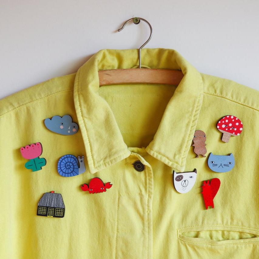 A yellow Donna Wilson jacket decorated with colorful wooden pins, including a blue cloud and red mushroom.