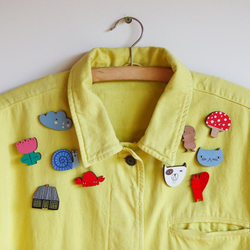 Yellow jacket by Donna Wilson adorned with colorful brooches: blue, pink, red, and green designs.