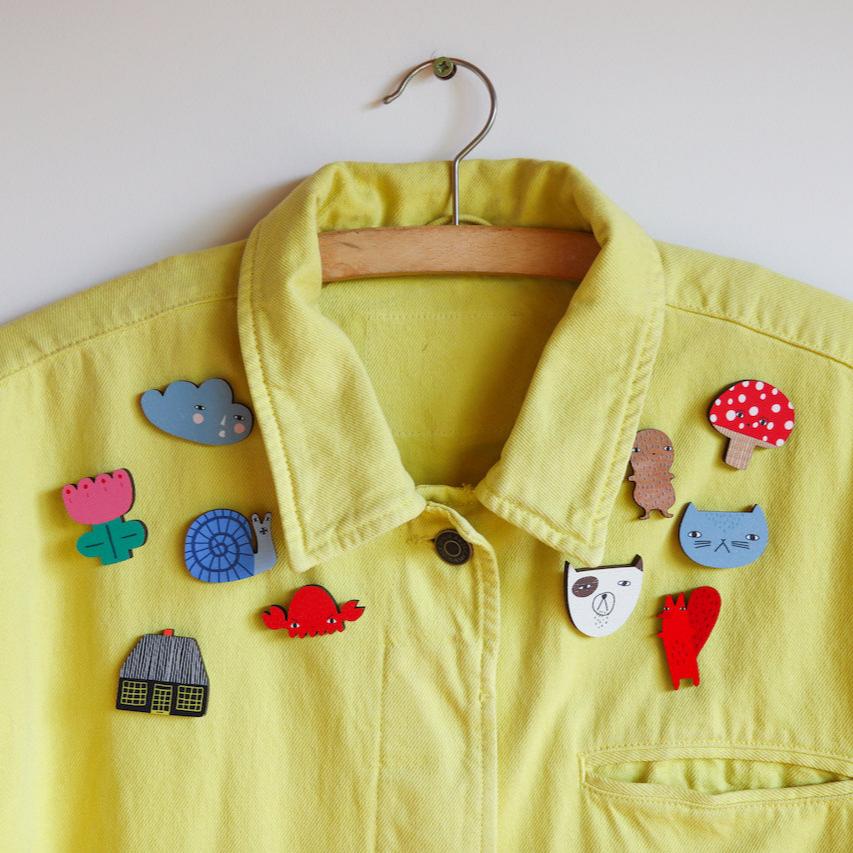 A yellow Donna Wilson jacket adorned with colorful, whimsical brooches featuring animals and plants.