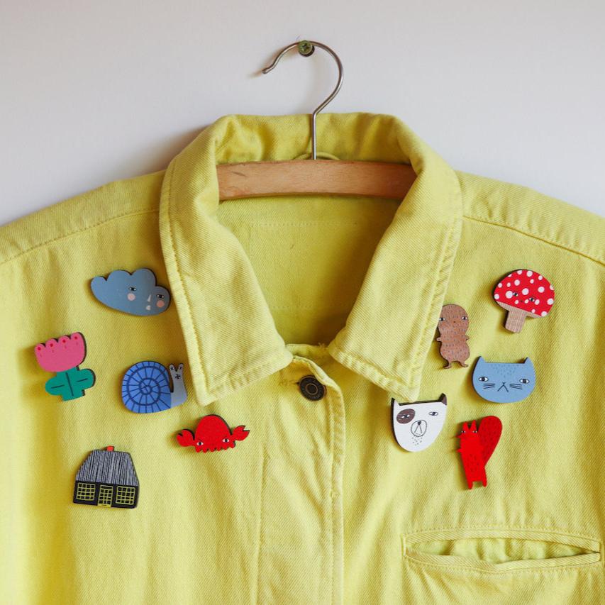Yellow jacket by Donna Wilson adorned with colorful pins: blue cloud, pink flower, green cactus, red mushroom, and more.