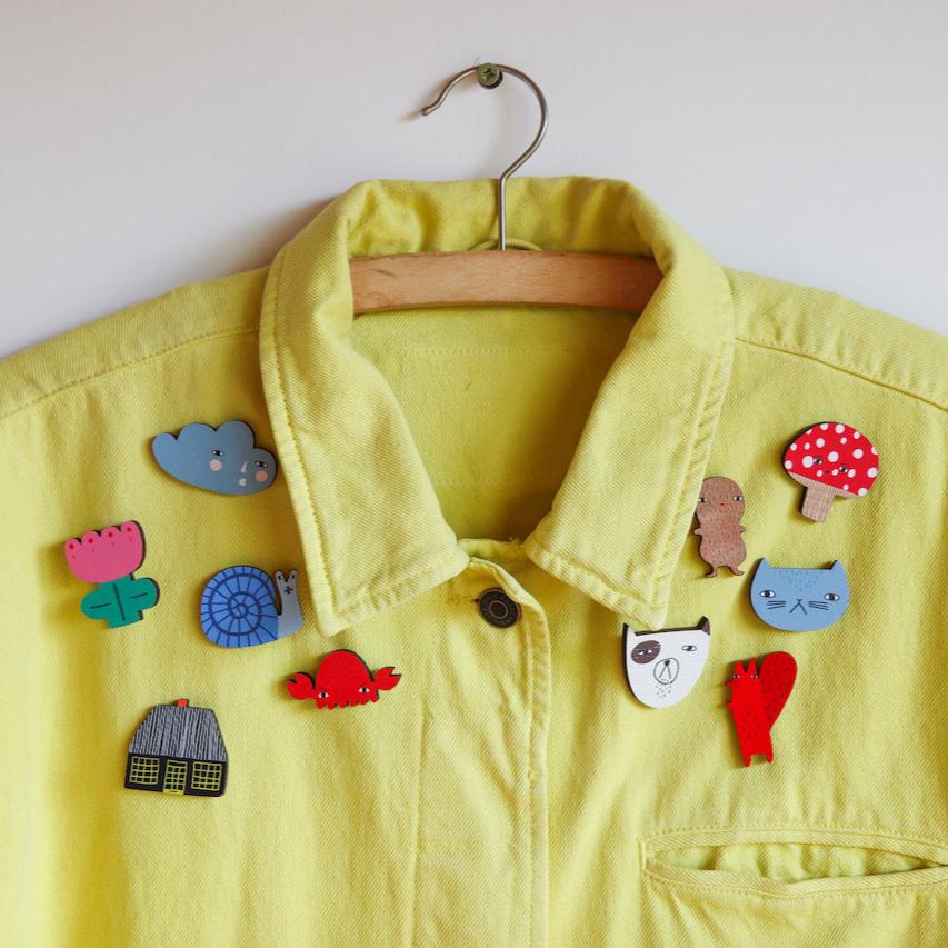 Yellow Donna Wilson jacket adorned with colorful pins including clouds, animals, and a mushroom.