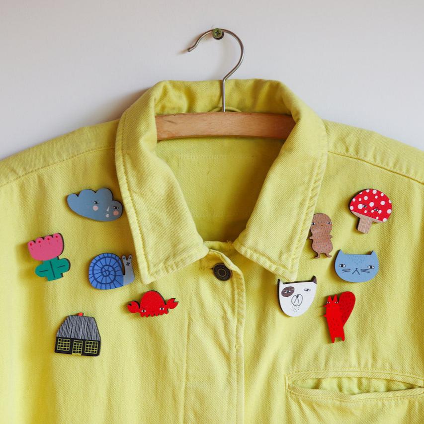 A yellow Donna Wilson jacket adorned with colorful, whimsical wooden brooches.