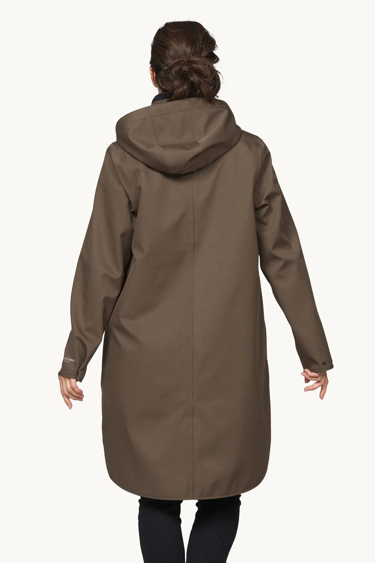 A woman viewed from the back wearing a mid-length hooded coat in a muted taupe-brown color, paired with dark leggings, against a plain light background.