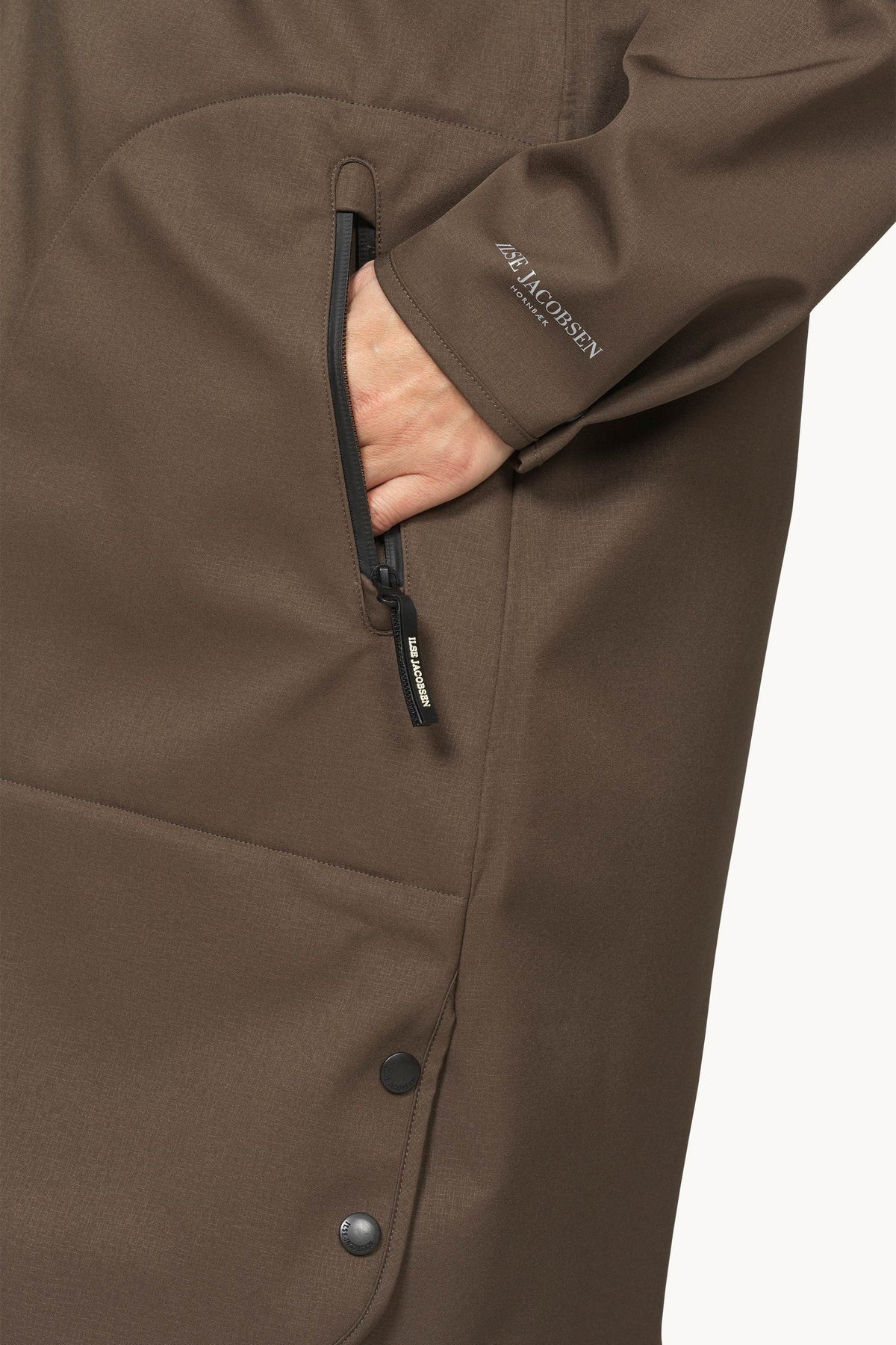 Close-up of a brown Salomon jacket with a hand in a zippered pocket, showing the Salomon logo on the sleeve.