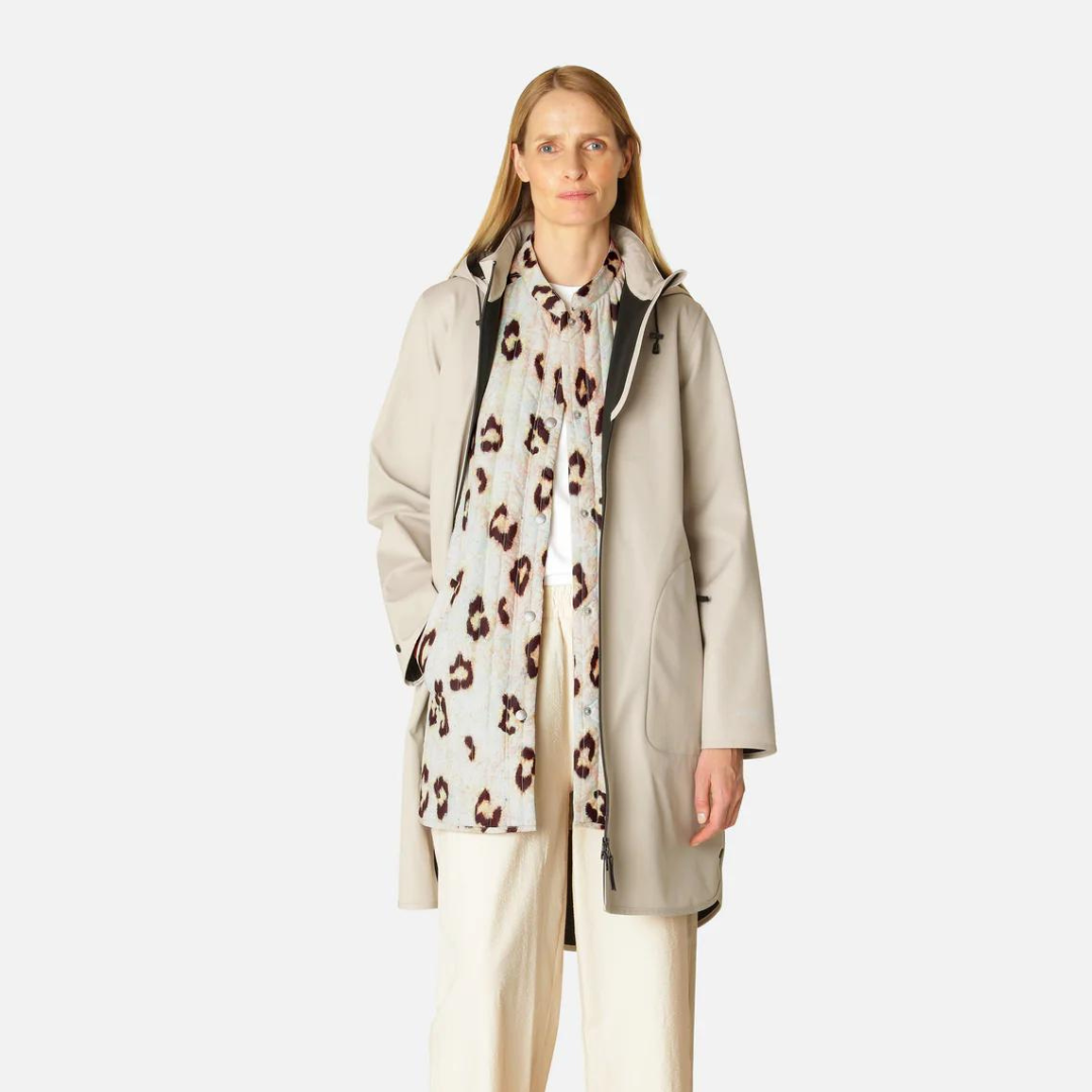 Beige raincoat with a leopard print scarf, worn by a blonde woman against a white background. The coat has a relaxed fit and a
