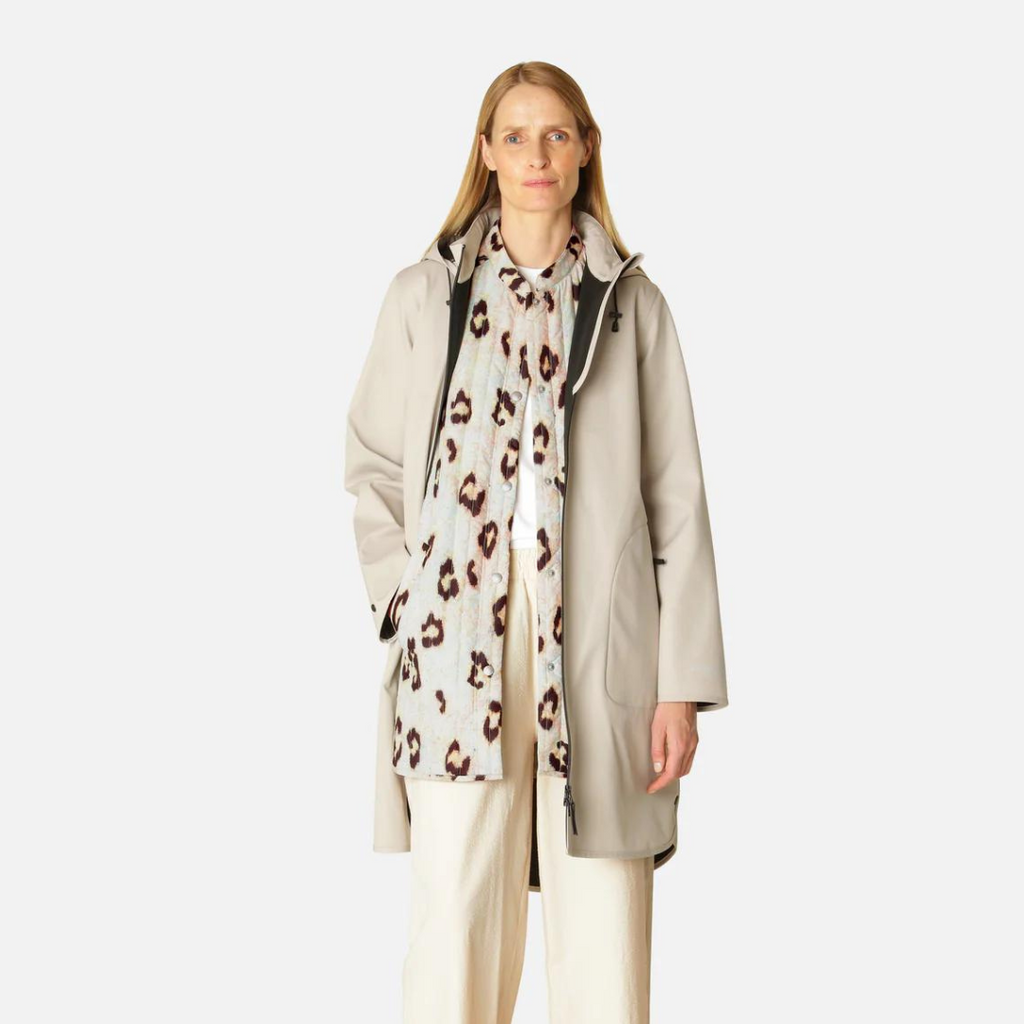 Beige raincoat with a leopard print scarf, worn by a blonde woman against a white background. The coat has a relaxed fit and a
