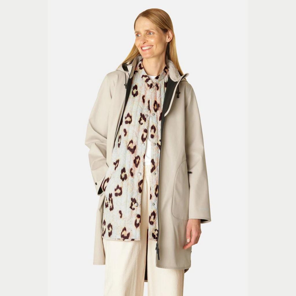 Beige raincoat with a hood, worn over a pale blue and brown animal print quilted shirt. The model is a fair-skinned woman with