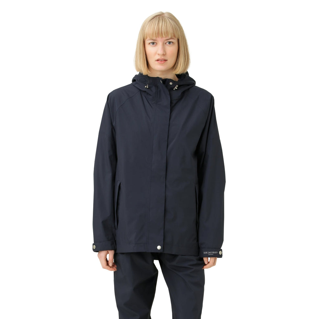 Woman in navy Ilse Jacobsen Hornbæk hooded raincoat and matching trousers. Smooth, matte fabric. Simple, minimalist design.