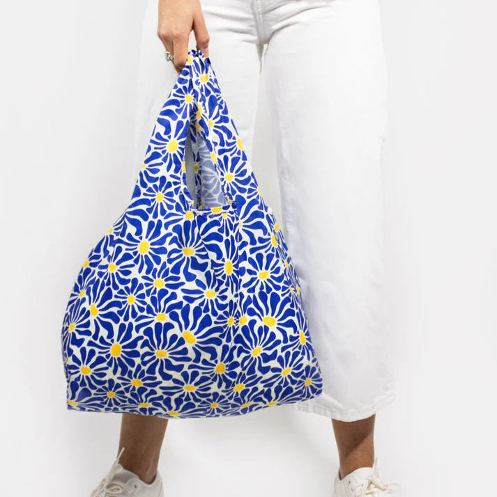 Reusable shopping bag with a blue and yellow daisy print.  The bag is folded and held by a person.