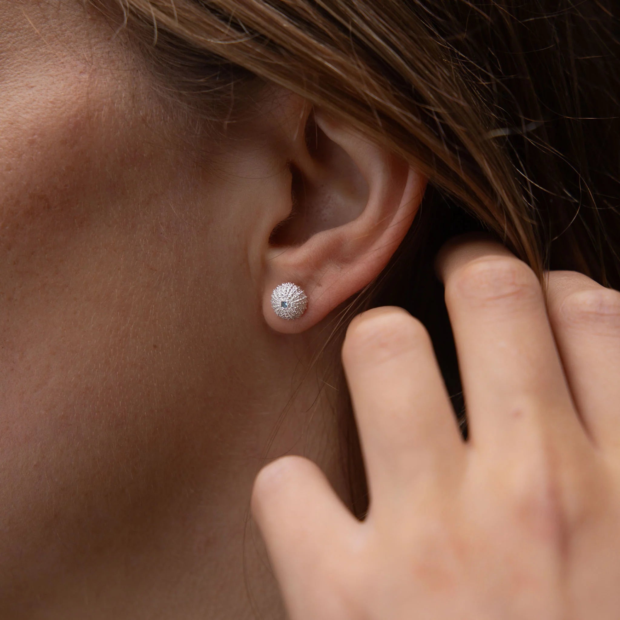 Close-up of an ear wearing a diamond stud earring with a hand adjusting it.