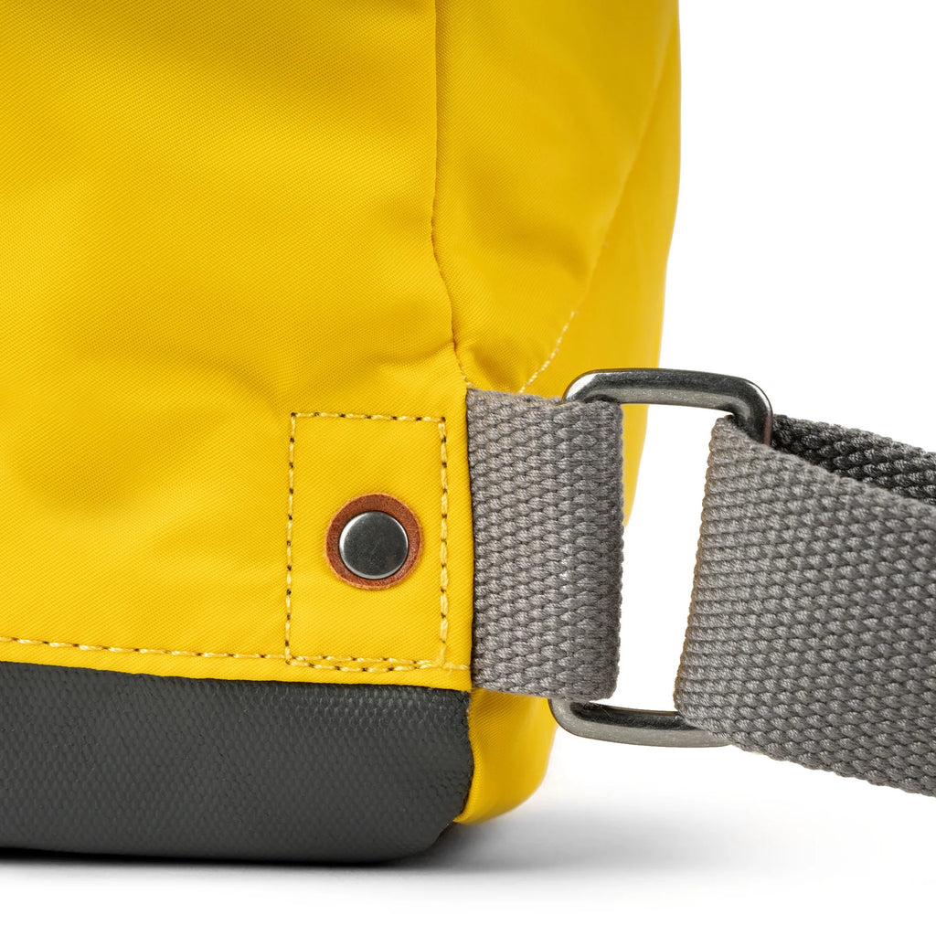 Close-up of a mustard-yellow bag's shoulder strap attachment.