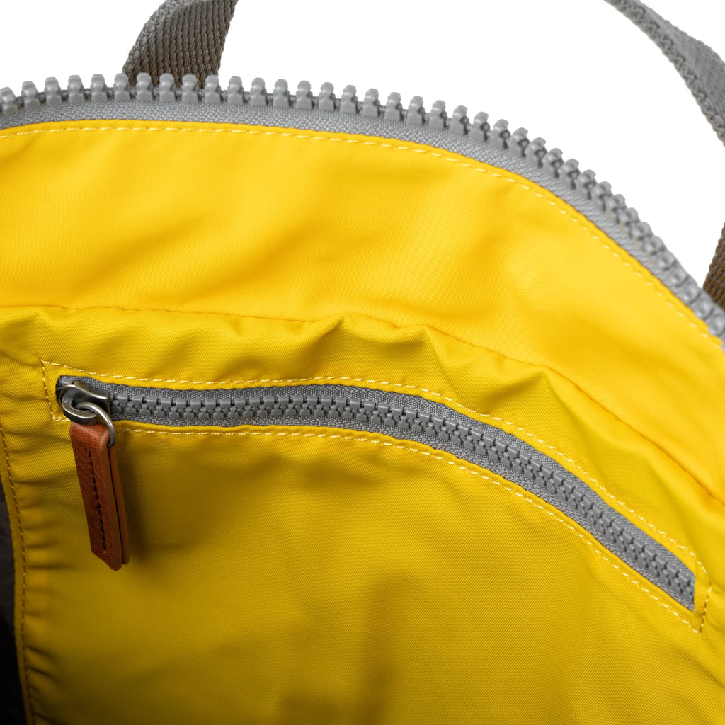 Close-up of a yellow bag's interior, showing a gray zipper and a small, tan leather zipper pull.