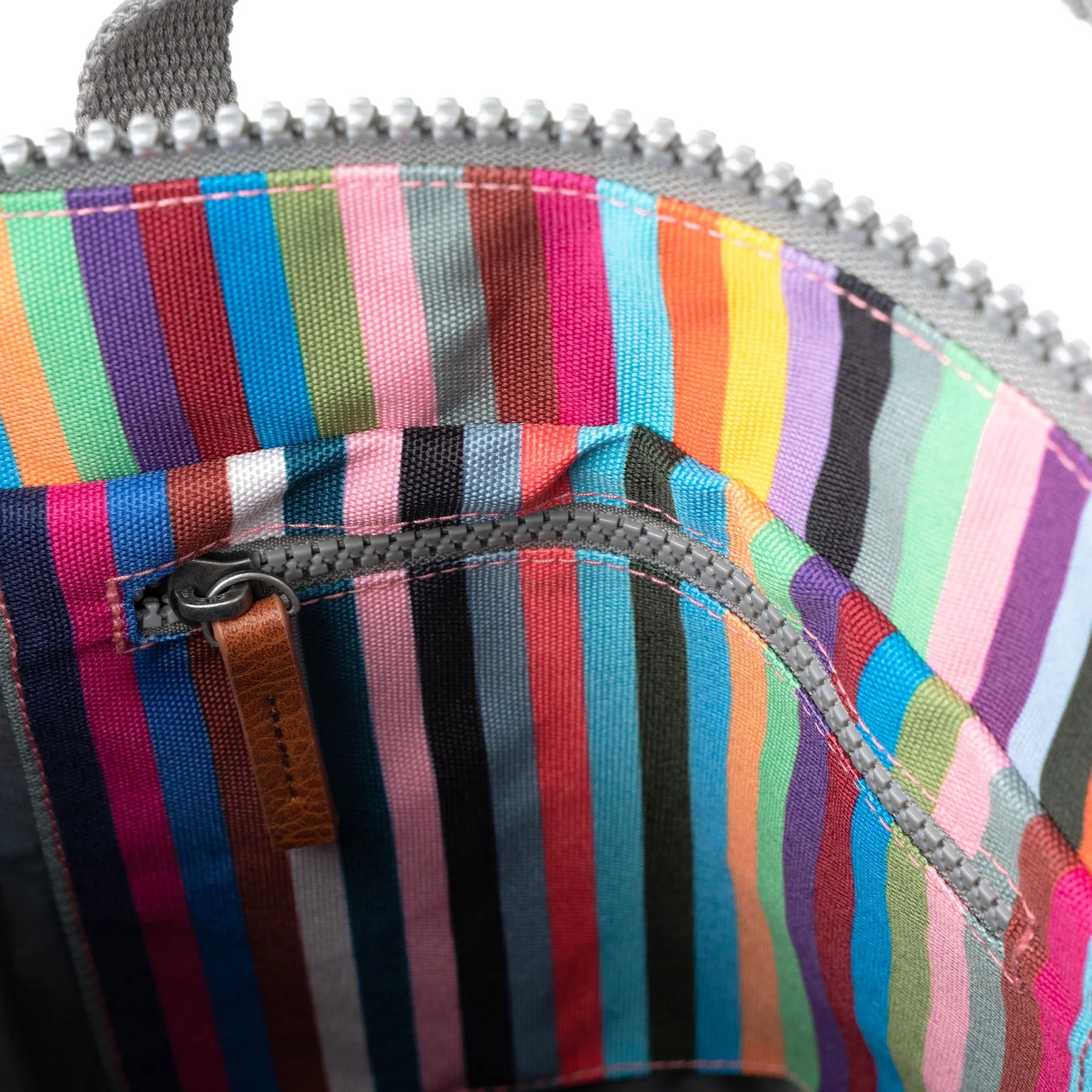 Inside of a multicolored striped bag with a gray zipper and a small brown leather pull tab.