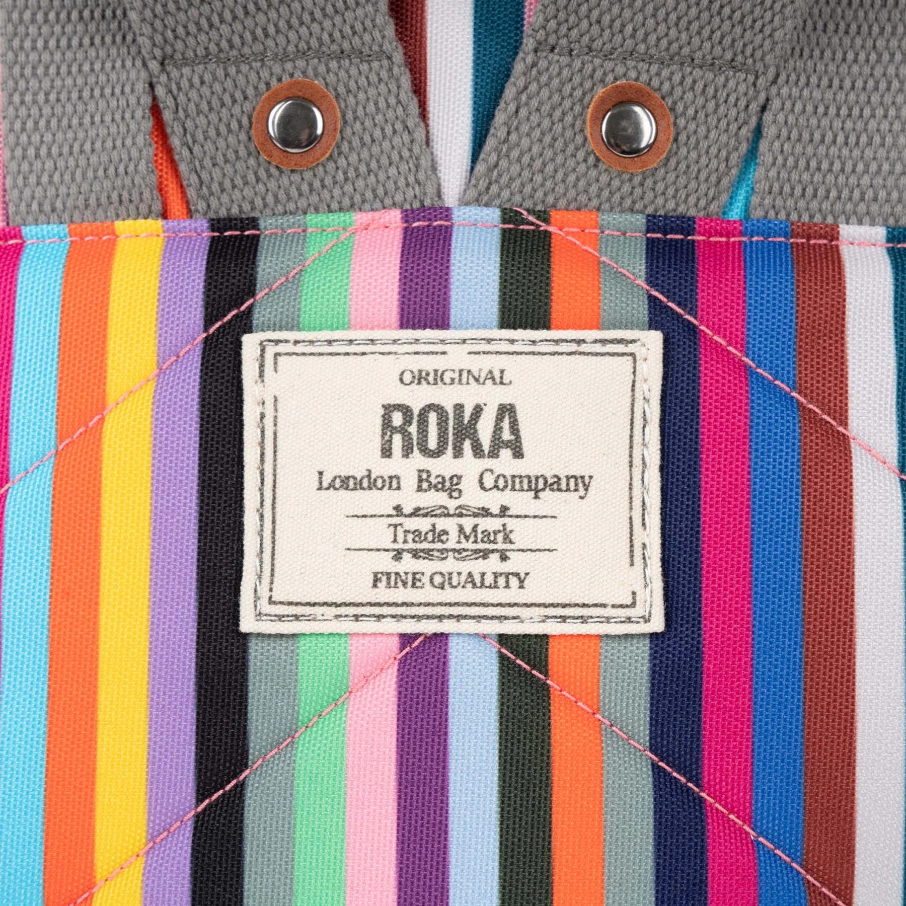 Close-up of a ROKA London Bag Company label on a multicolored striped fabric bag.