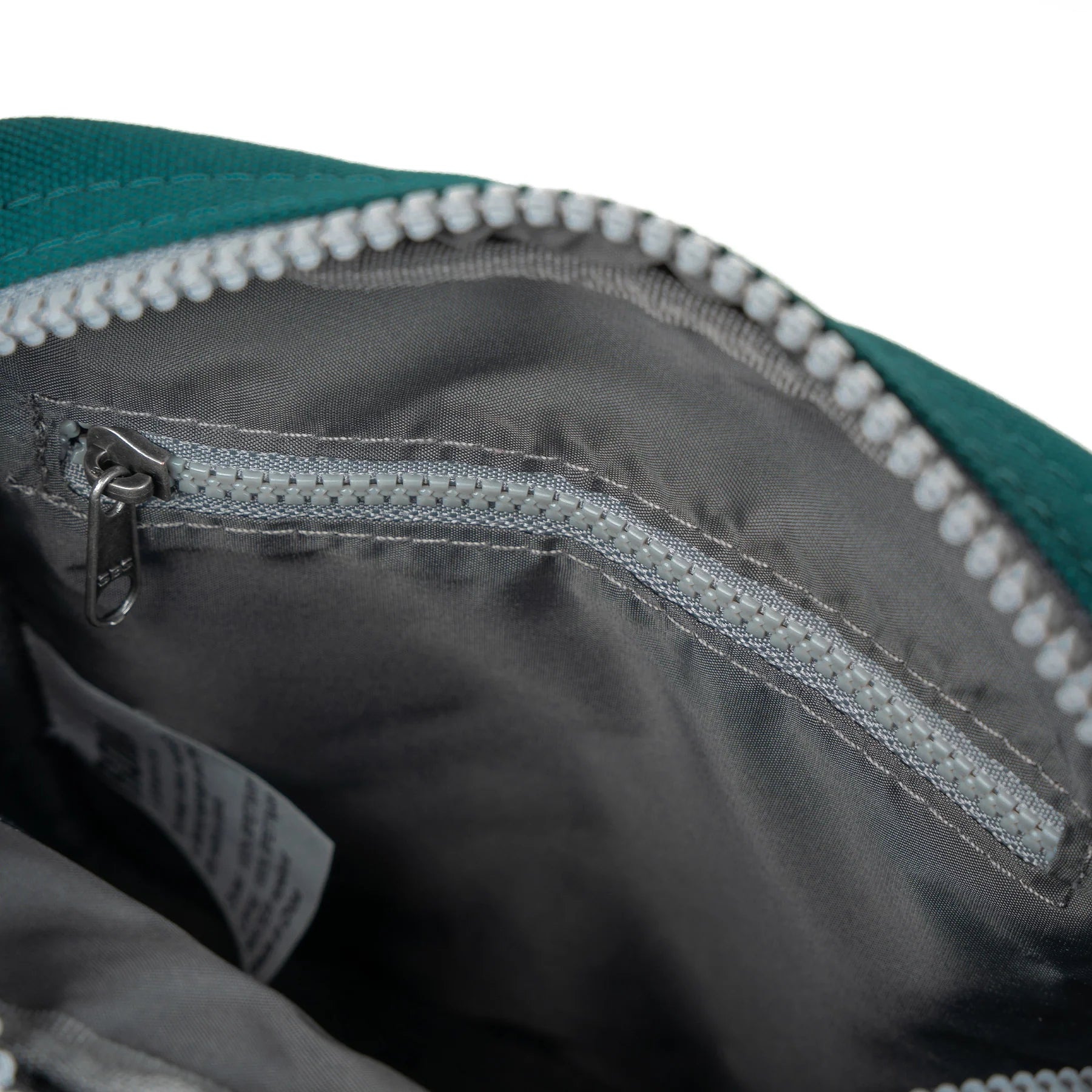 A teal Bond Pocket Crossbody bag made from recycled canvas with a zippered top, an extra external pocket, and an adjustable strap. It features a main compartment and an additional mesh pocket inside.