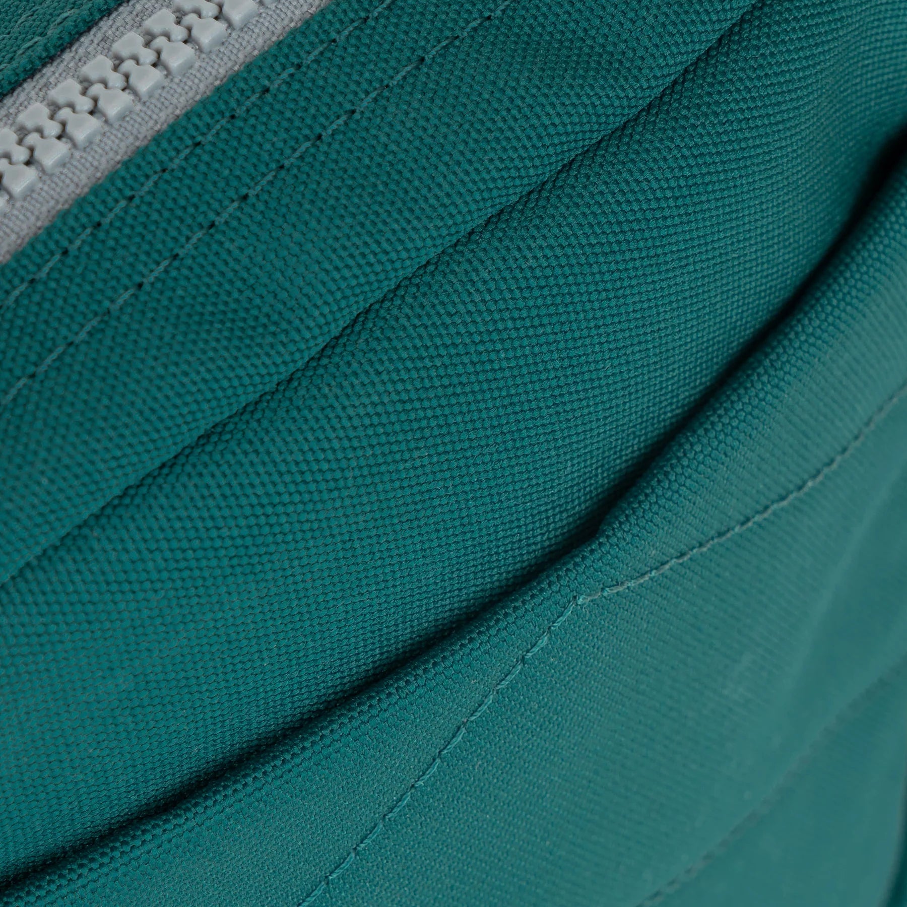 A teal Bond Pocket Crossbody bag made from recycled canvas with a zippered top, an extra external pocket, and an adjustable strap. It features a main compartment and an additional mesh pocket inside.