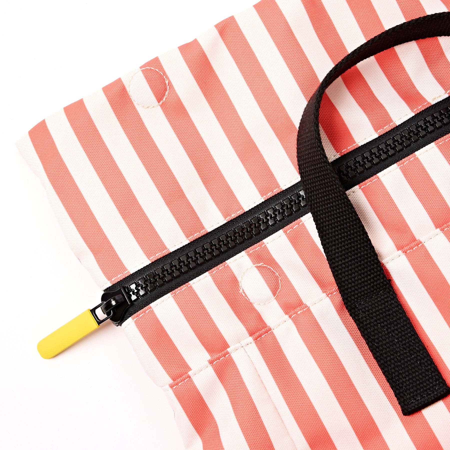 Close-up of a bag with a black zipper and strap on a red and white striped background