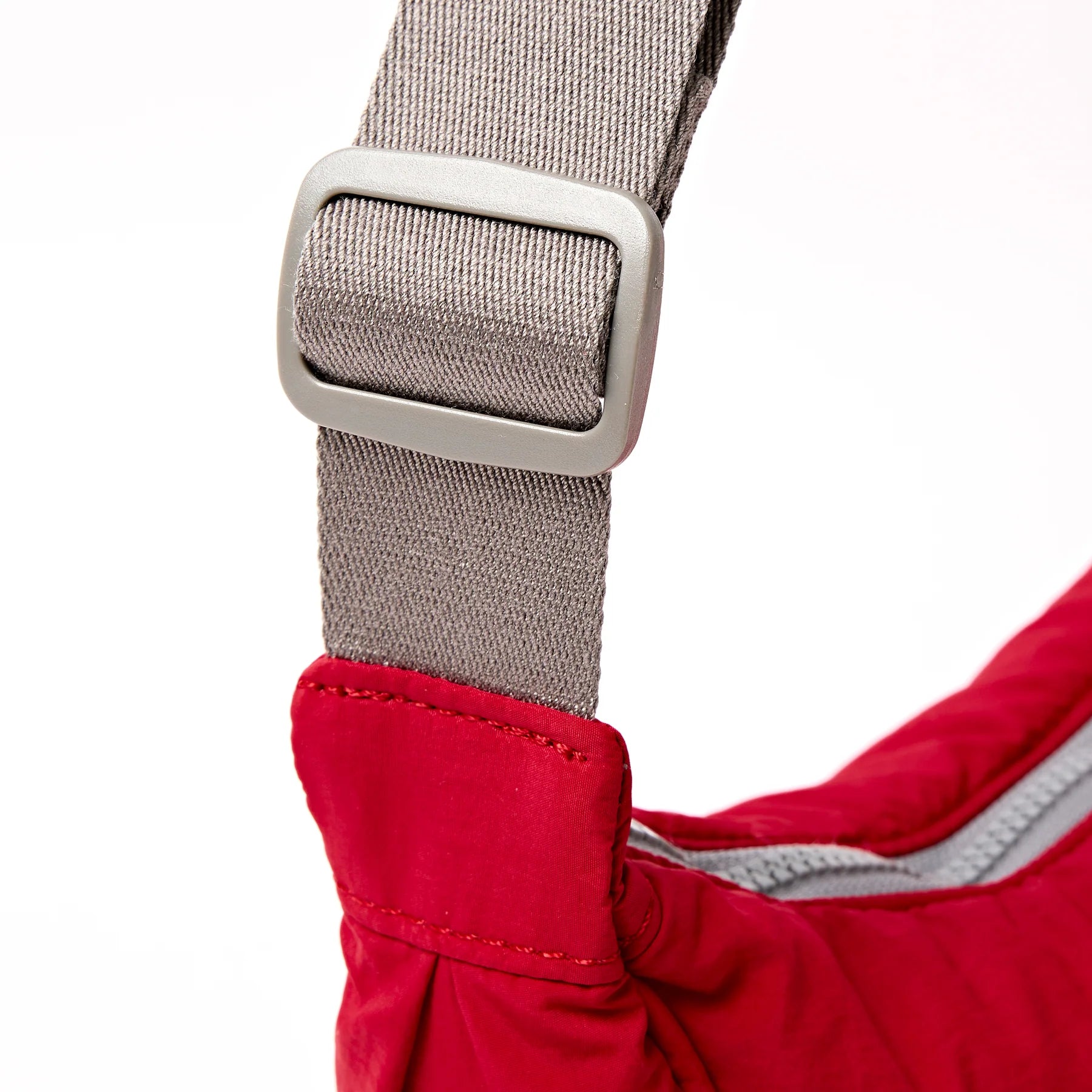 Close-up of a red jacket with a gray strap and buckle on a white background