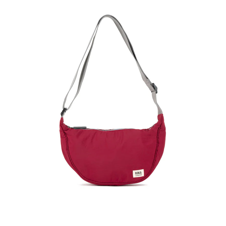 Red crescent-shaped crossbody bag with gray shoulder strap and small label.
