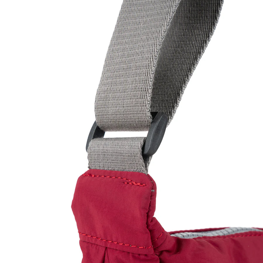 Close-up of a red handbag's shoulder strap, showing a grey fabric strap with black plastic adjusters.