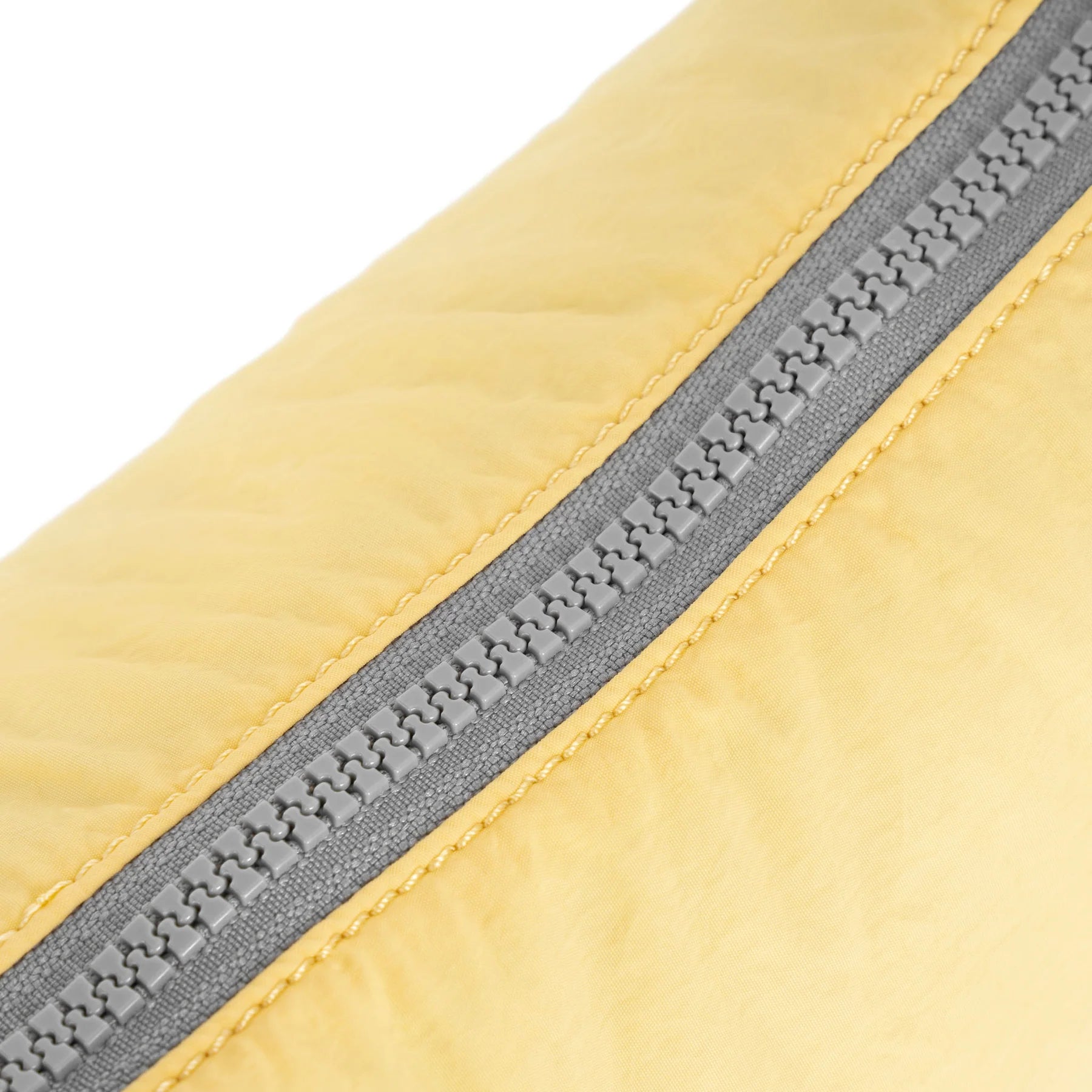 Close-up detail of a light yellow quilted fabric item with a gray zipper running diagonally across the frame.