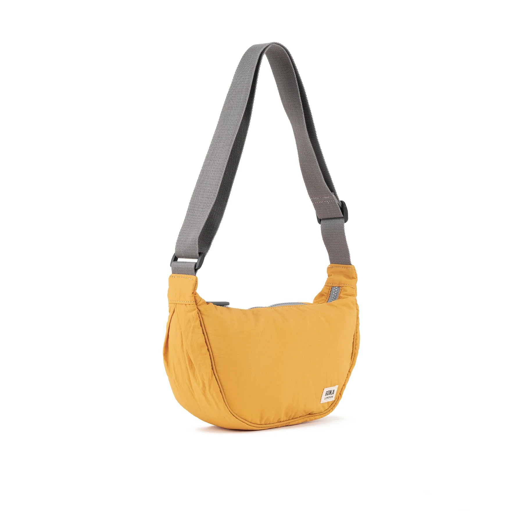 Mustard-yellow crossbody bag with gray straps and a zipper closure. The bag is slightly curved and has a quilted texture.