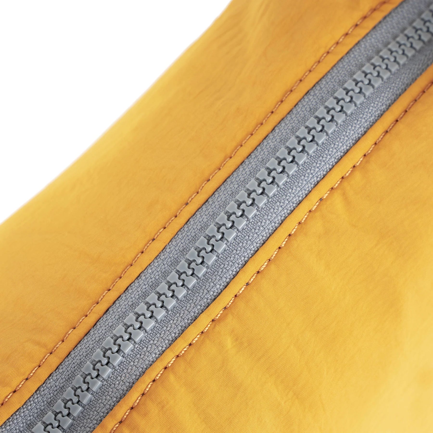 Close-up of a gray zipper on mustard-yellow fabric. The zipper teeth are clearly visible, and the fabric is subtly textured.