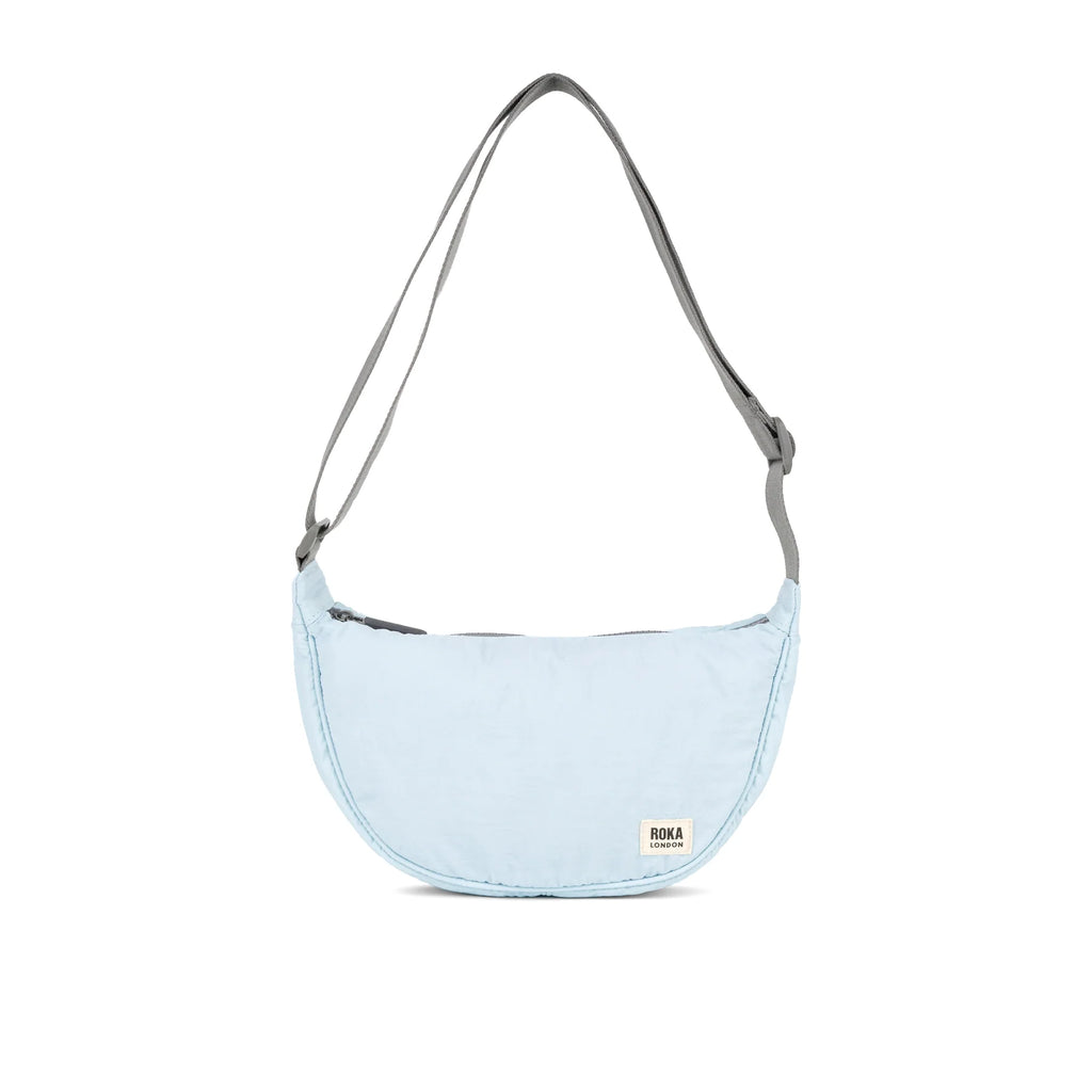 Light blue ROKA bag with a curved shape and grey strap, featuring a zip closure and brand label.