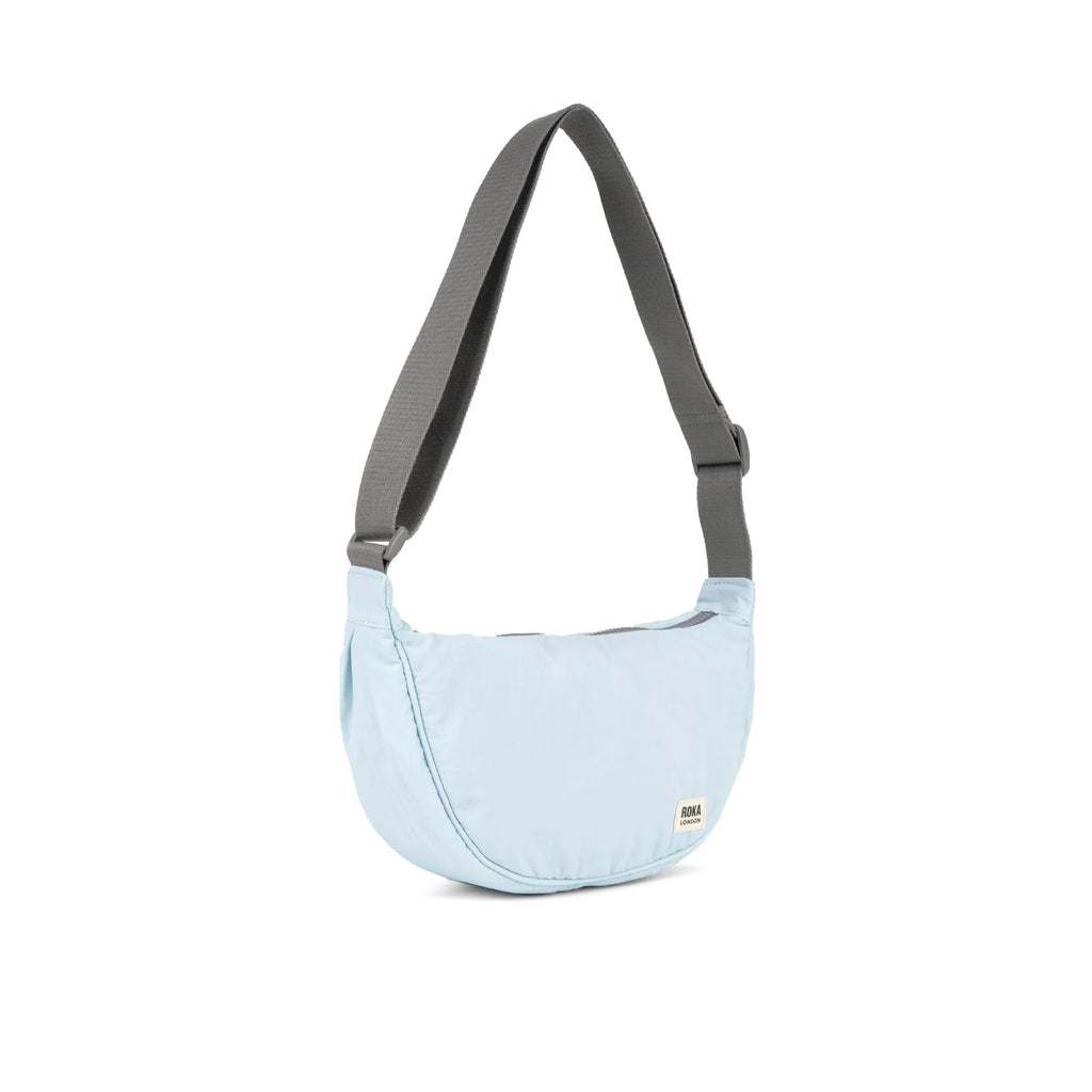 Light blue ROKA sling bag with a gray strap, featuring a minimalist design and a compact shape.