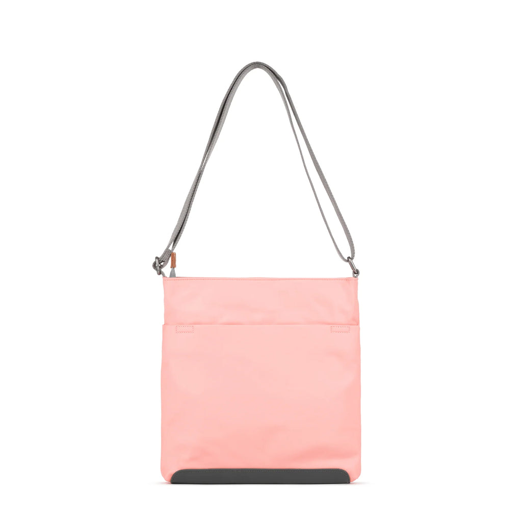 ROKA pink crossbody bag with a grey strap, featuring a sleek design and front pocket for easy access.