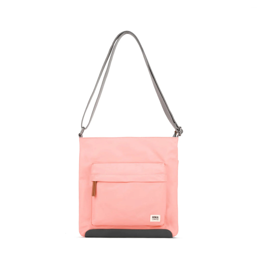 ROKA pink crossbody bag with a front pocket and gray strap on a white background.