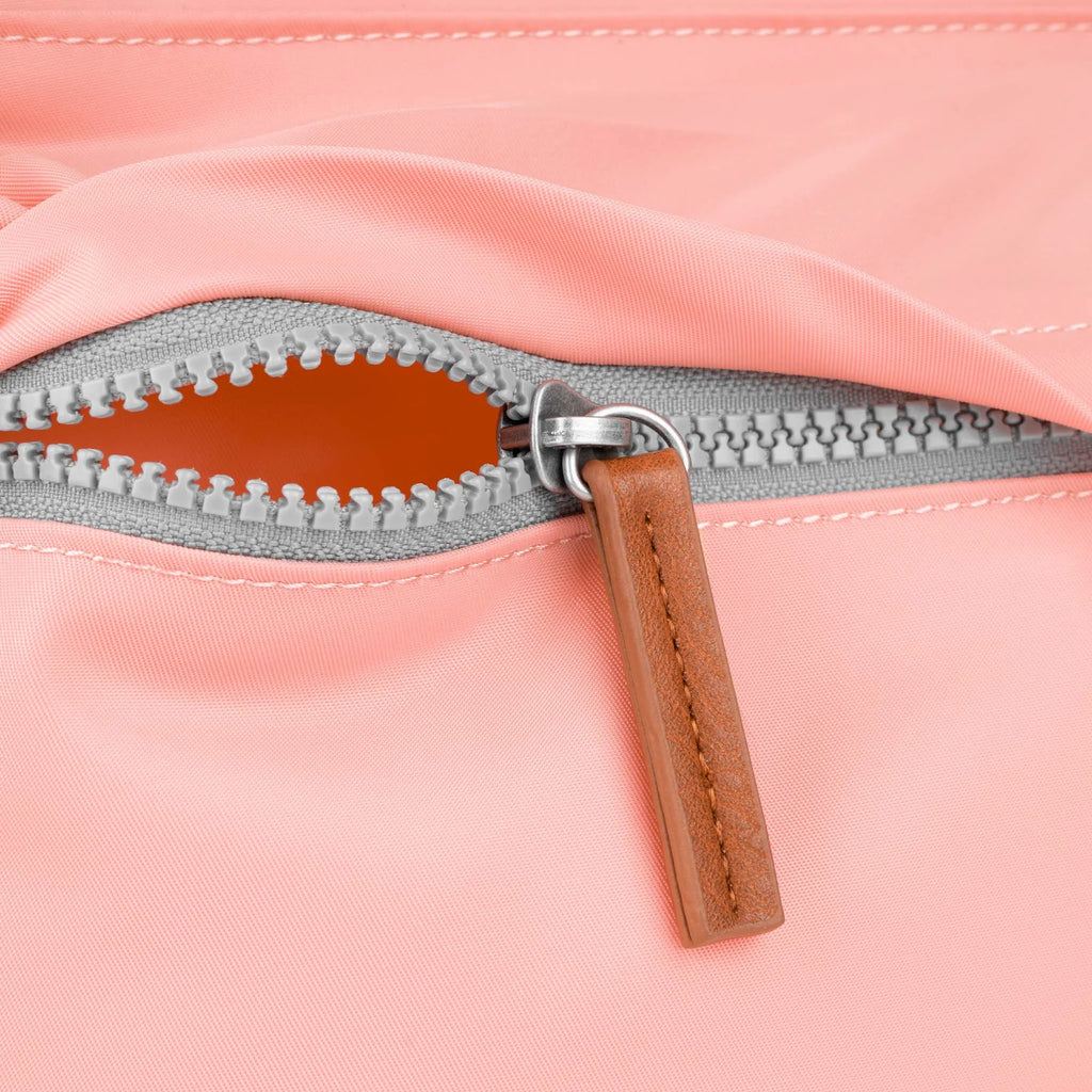 Close-up of a pink ROKA bag zipper with a leather pull tab and grey stitching.
