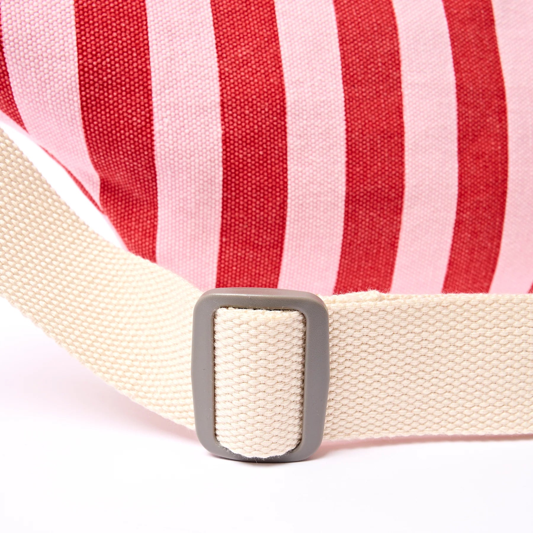 Close-up of a red and pink striped fabric with a beige strap and silver buckle on a white background.
