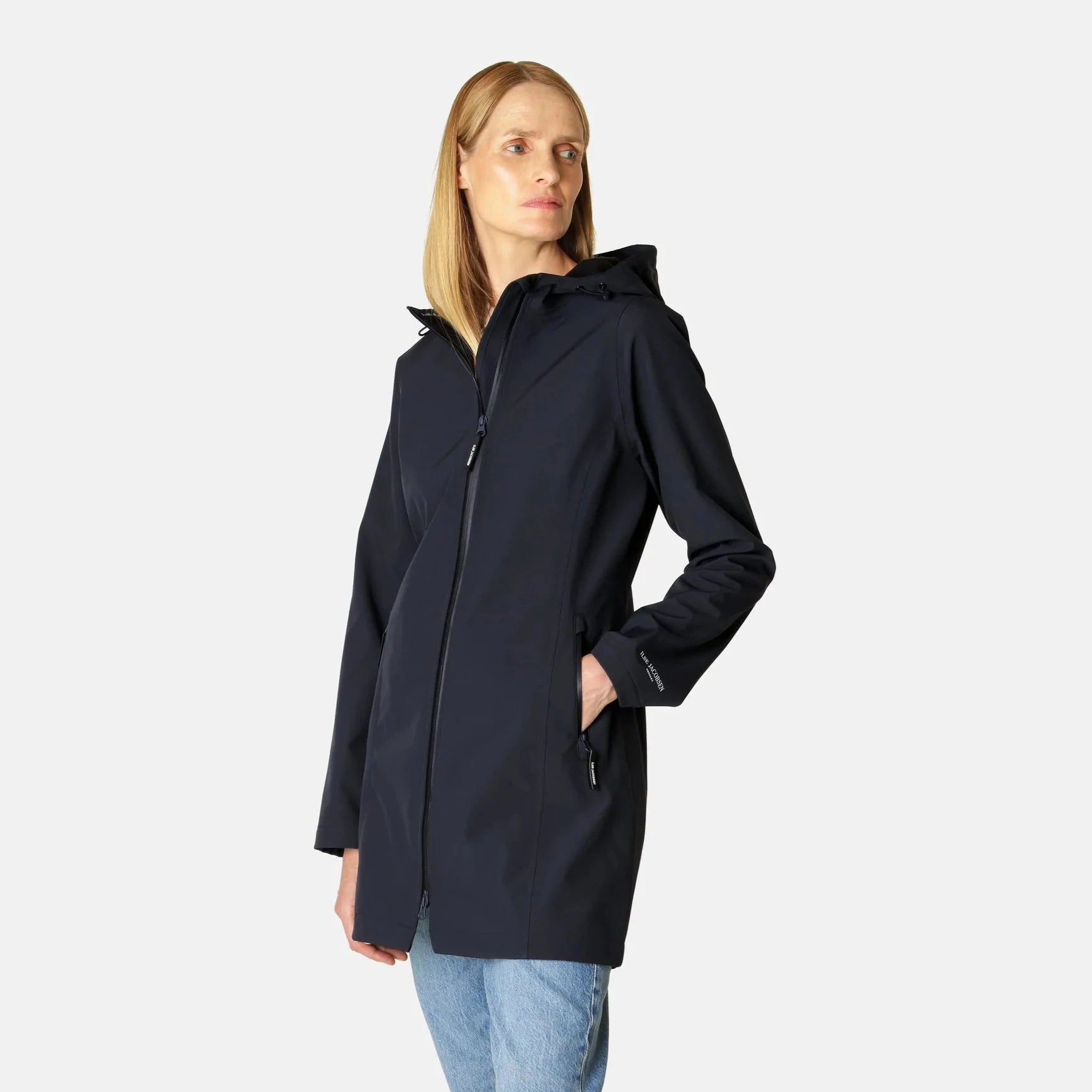 Woman in navy blue, zip-up, hooded Ilse Jacobsen raincoat; smooth, matte texture; long sleeves, pockets.