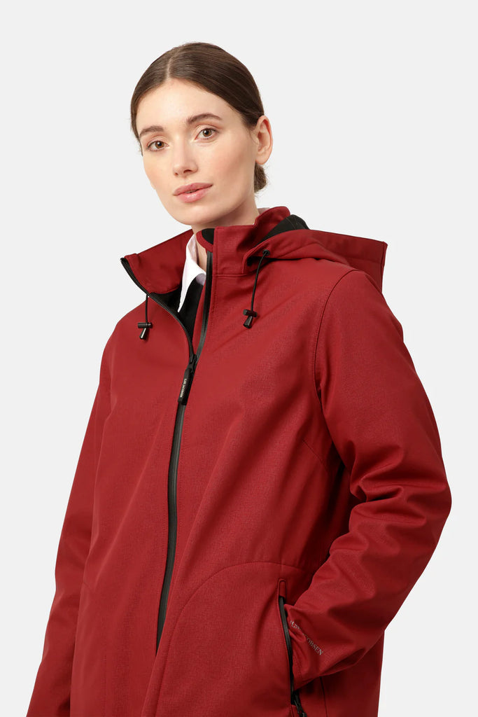 Woman modeling a burgundy softshell jacket with a black hood and zipper. The jacket has subtle texture and a relaxed fit.