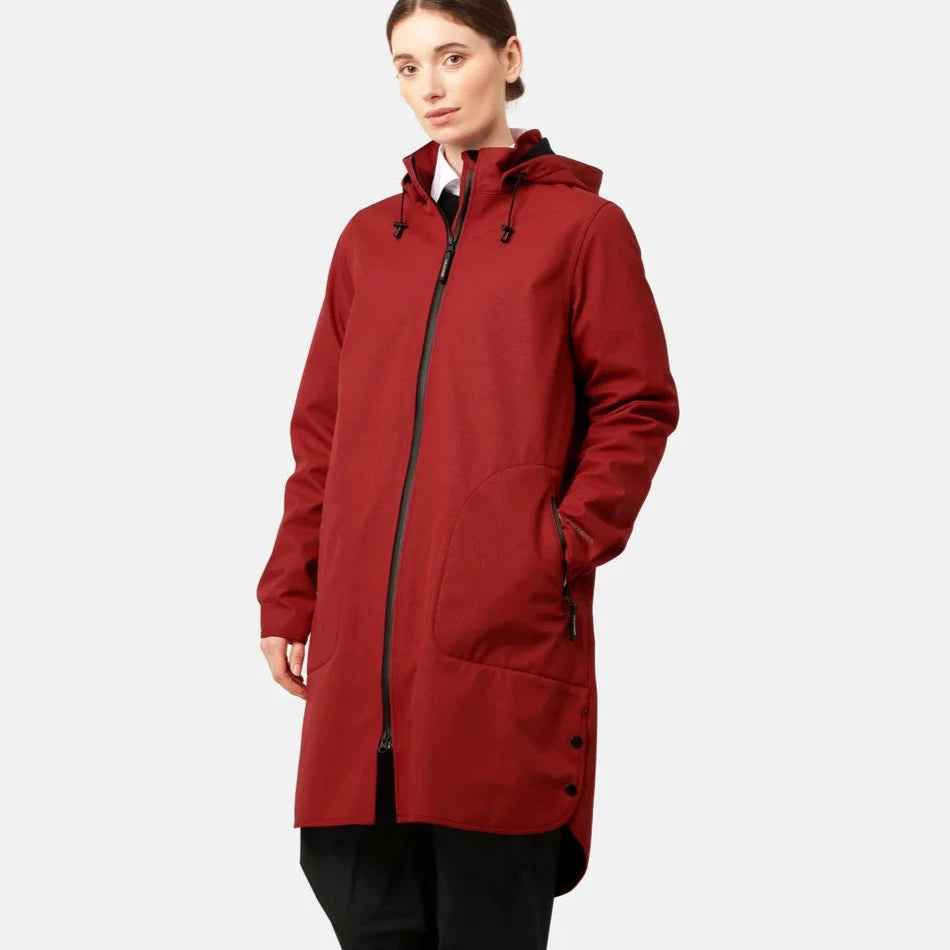 Red waterproof Rains long coat with a zip-up front, pockets, and a curved hem. Model wears black pants.