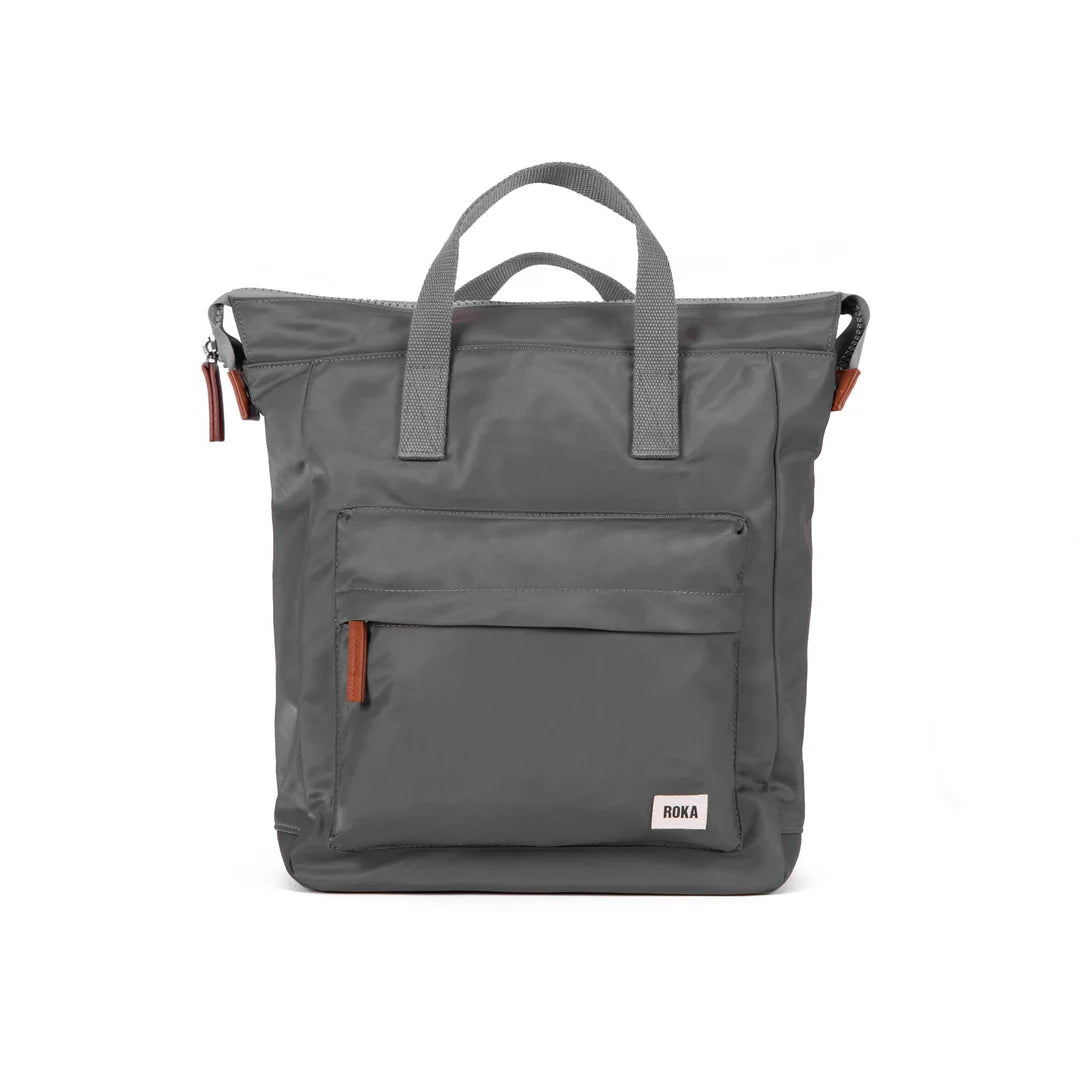Grey convertible backpack with top handles and a front pocket; features brown leather zipper pulls and a small "ROKA" label.
