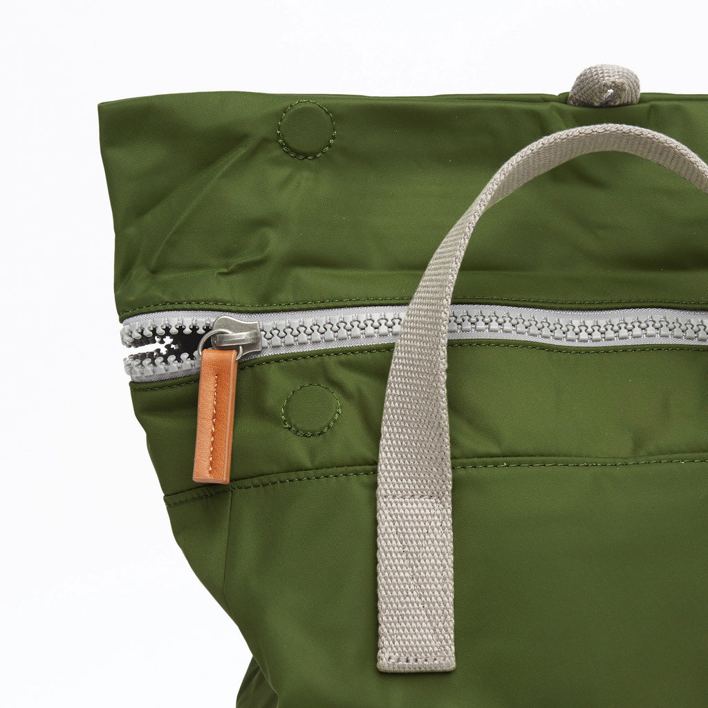 Olive green nylon tote bag with silver zipper, tan leather zipper pull, and light gray fabric handles.