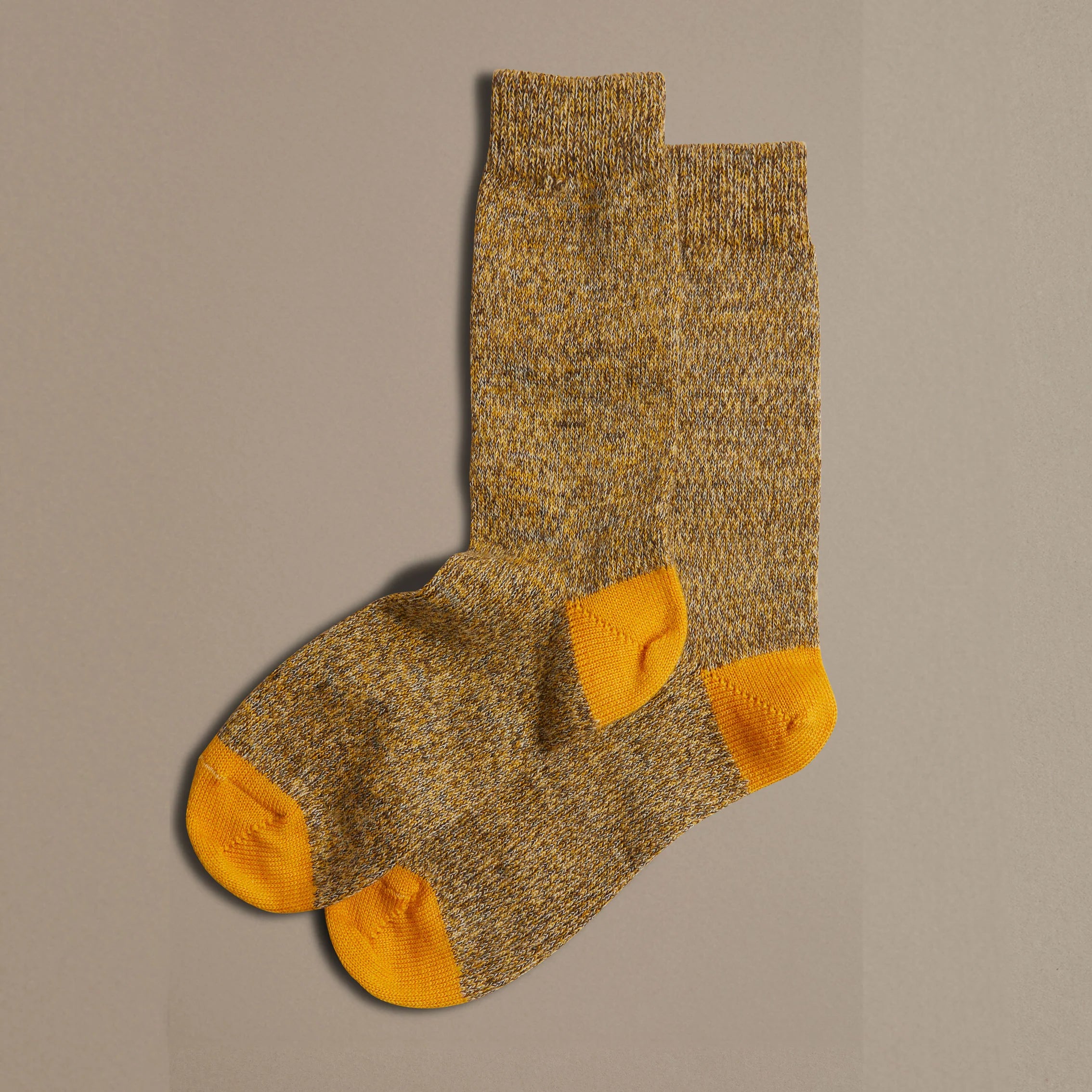 Pair of mustard yellow crew socks with orange heels and toes.  The socks have a speckled texture.
